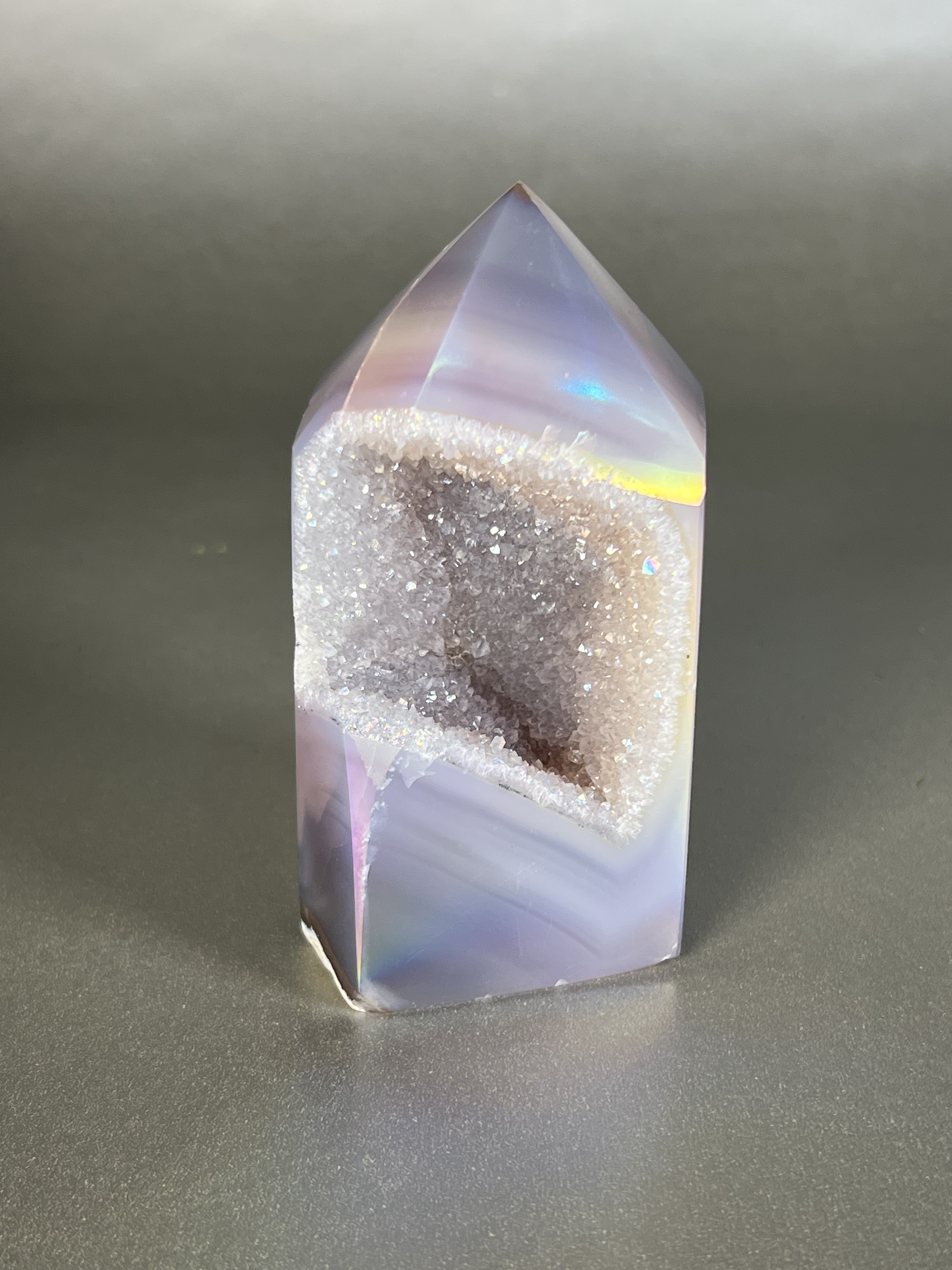 Experience the dreamy elegance of our Aura Agate Obelisk. Each one is uniquely crafted to exude a sense of luxury and exclusivity. Featuring the rare Aura Agate stone, this obelisk brings a touch of sophistication and beauty to any space. Elevate your decor with this truly one-of-a-kind piece. Approx. 2" x 4" Aura Agate Tower