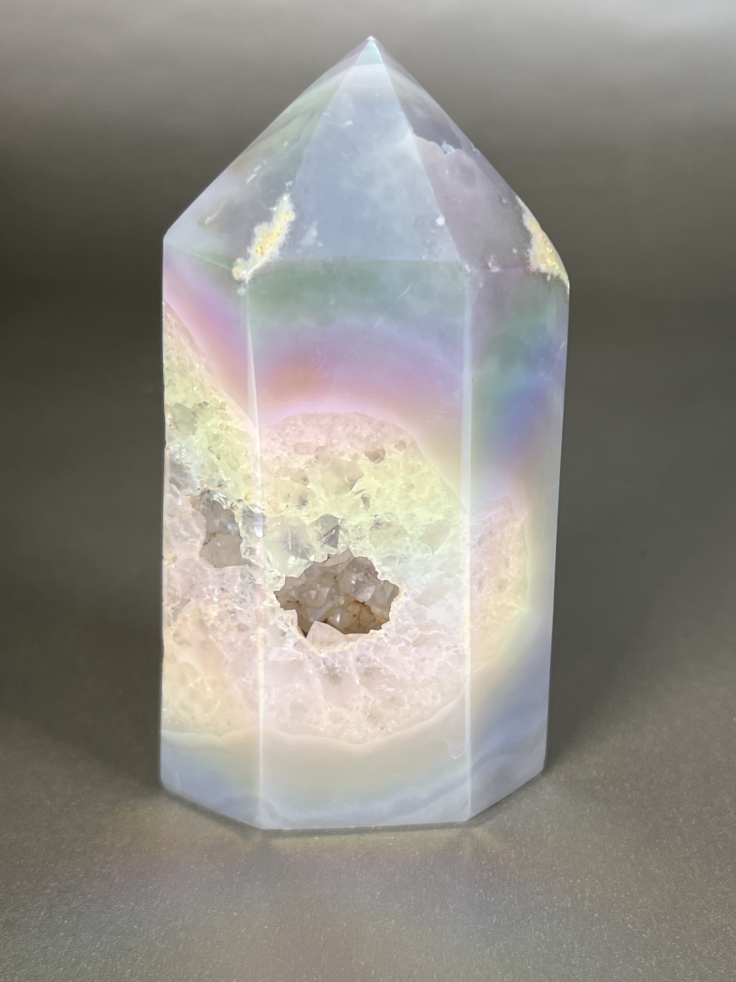 Experience the dreamy elegance of our Aura Agate Obelisk. Each one is uniquely crafted to exude a sense of luxury and exclusivity. Featuring the rare Aura Agate stone, this obelisk brings a touch of sophistication and beauty to any space. Elevate your decor with this truly one-of-a-kind piece. Approx. 2.5" x 5" Aura Agate Tower
