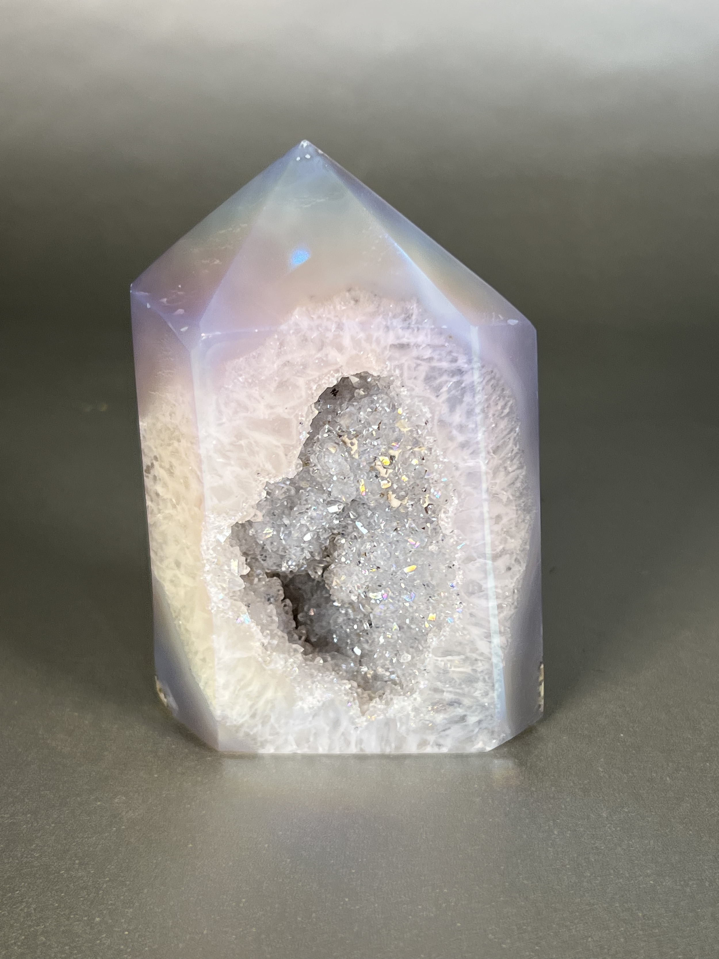 Experience the dreamy elegance of our Aura Agate Obelisk. Each one is uniquely crafted to exude a sense of luxury and exclusivity. Featuring the rare Aura Agate stone, this obelisk brings a touch of sophistication and beauty to any space. Elevate your decor with this truly one-of-a-kind piece. Approx. 3" x 4.5" Aura Agate Tower