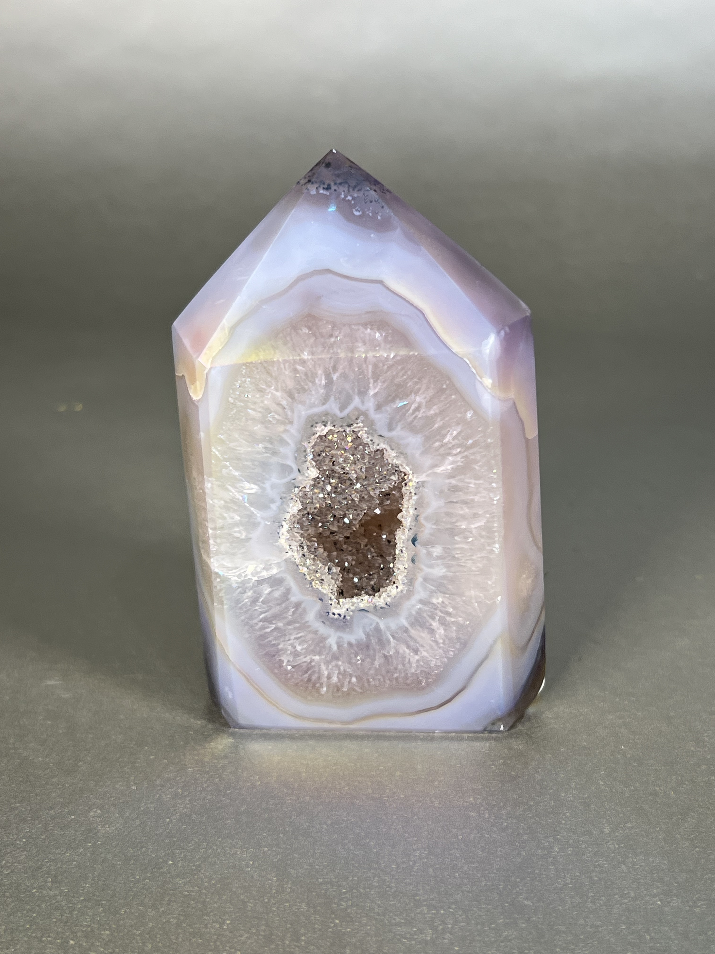 Experience the dreamy elegance of our Aura Agate Obelisk. Each one is uniquely crafted to exude a sense of luxury and exclusivity. Featuring the rare Aura Agate stone, this obelisk brings a touch of sophistication and beauty to any space. Elevate your decor with this truly one-of-a-kind piece. Approx. 2.5" x 4" Aura Agate Tower