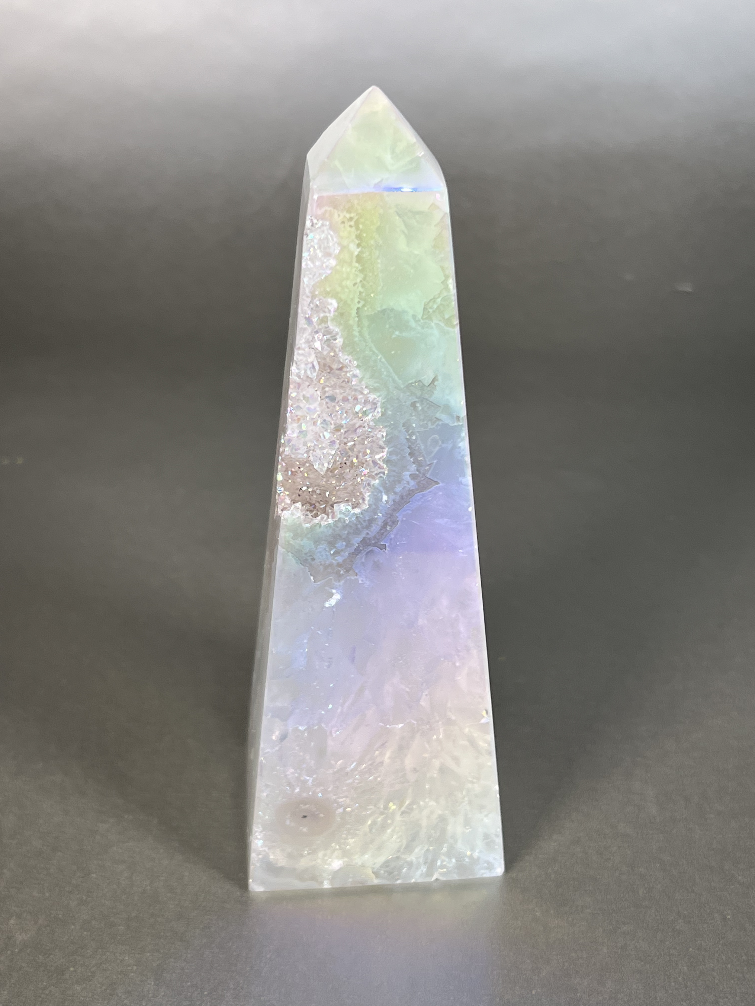 Experience the dreamy elegance of our Aura Agate Obelisk. Each one is uniquely crafted to exude a sense of luxury and exclusivity. Featuring the rare Aura Agate stone, this obelisk brings a touch of sophistication and beauty to any space. Elevate your decor with this truly one-of-a-kind piece. Approx. 2" x 6" Aura Agate Tower