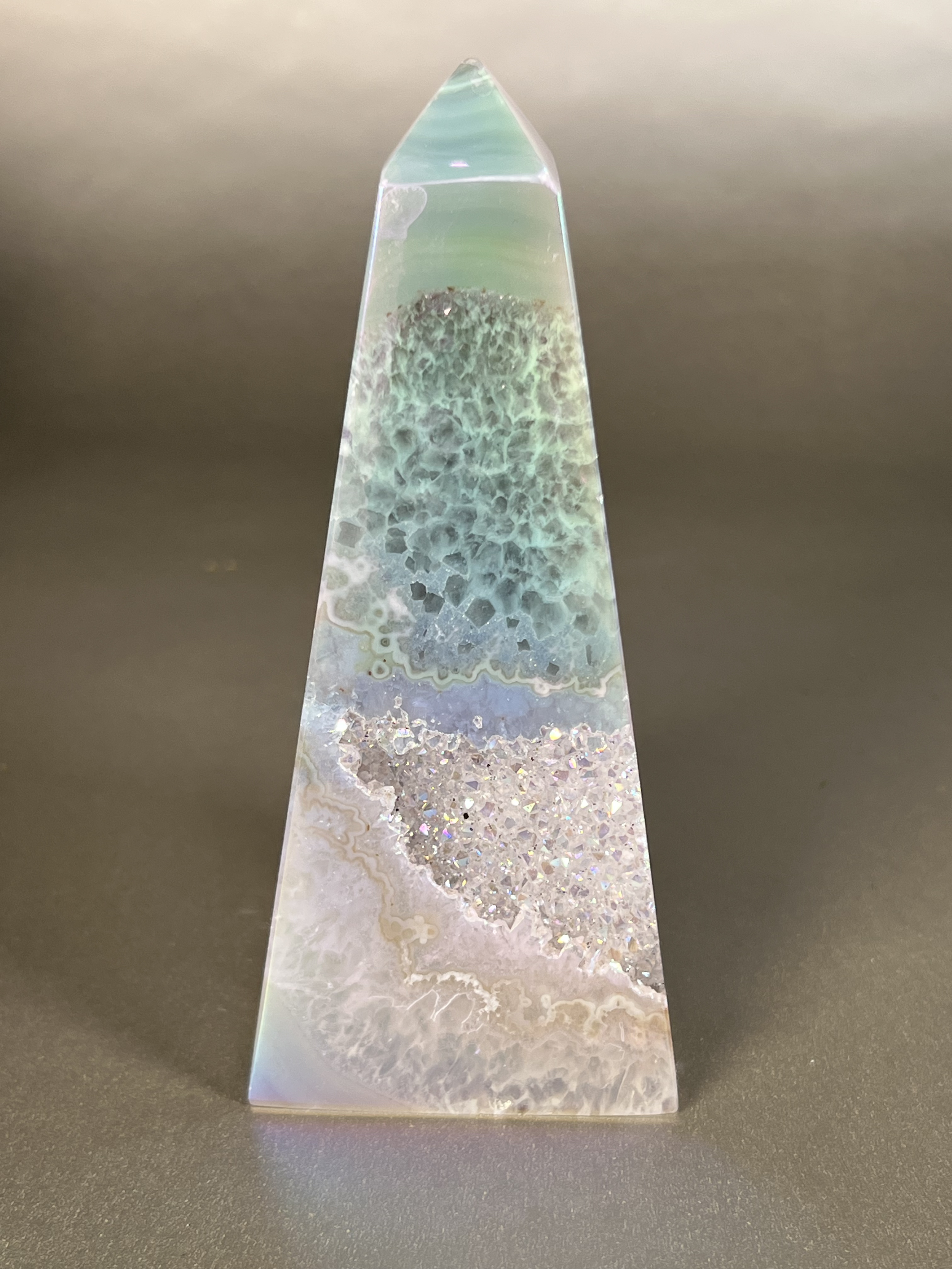 Experience the dreamy elegance of our Aura Agate Obelisk. Each one is uniquely crafted to exude a sense of luxury and exclusivity. Featuring the rare Aura Agate stone, this obelisk brings a touch of sophistication and beauty to any space. Elevate your decor with this truly one-of-a-kind piece. Approx. 2" x 5.5" Aura Agate Tower