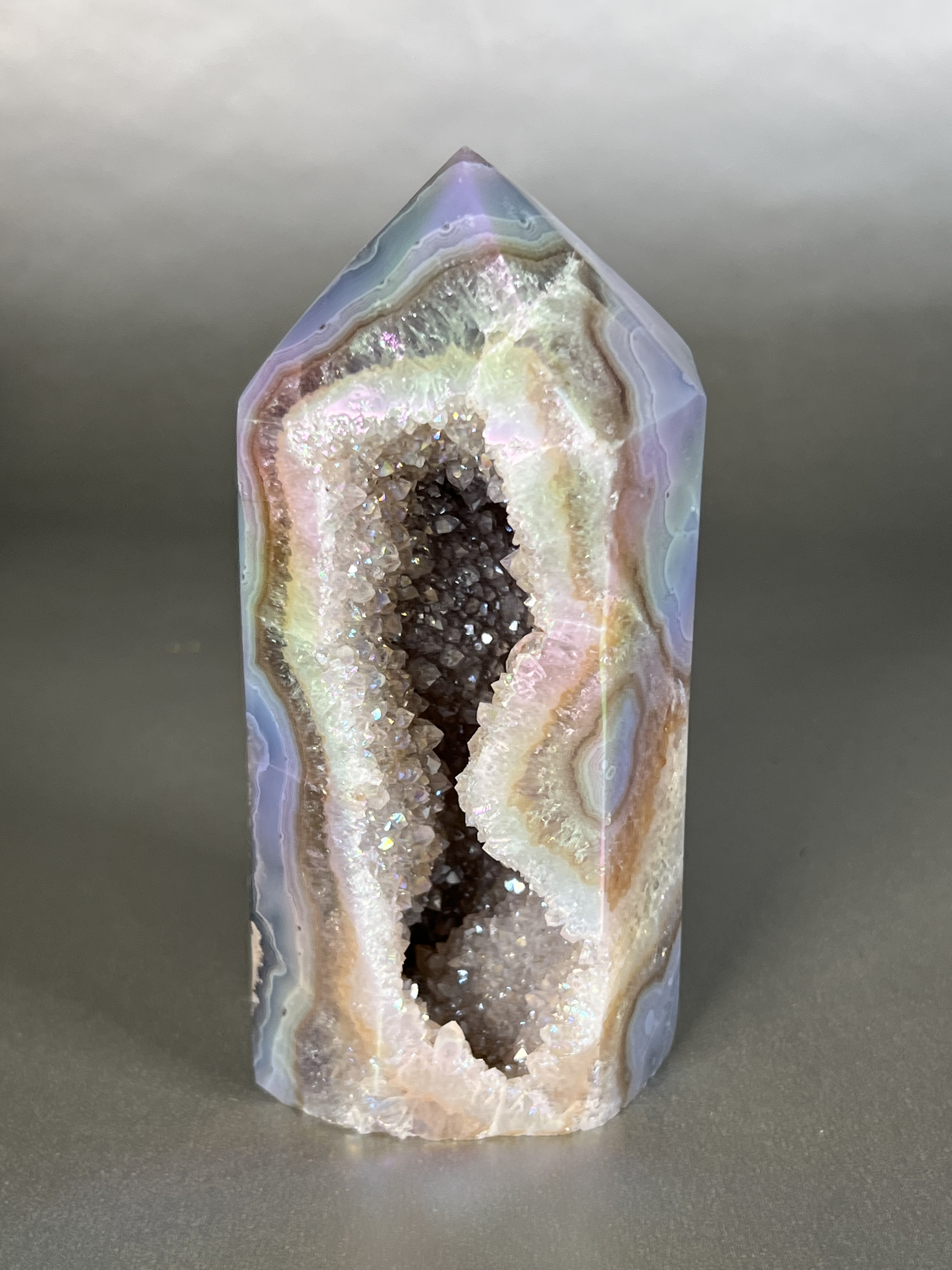 Experience the dreamy elegance of our Aura Agate Obelisk. Each one is uniquely crafted to exude a sense of luxury and exclusivity. Featuring the rare Aura Agate stone, this obelisk brings a touch of sophistication and beauty to any space. Elevate your decor with this truly one-of-a-kind piece. Approx. 2.5"x5.5" Aura Agate Tower