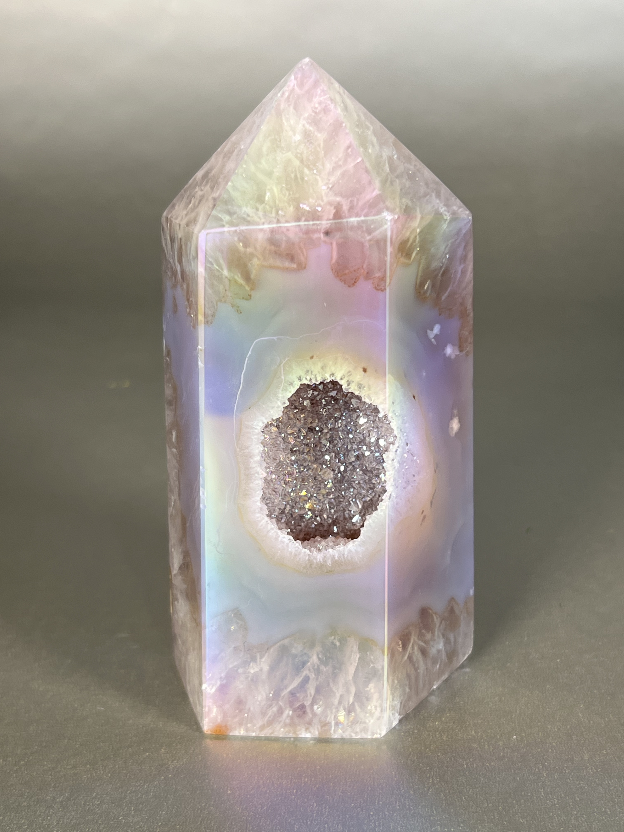 Experience the dreamy elegance of our Aura Agate Obelisk. Each one is uniquely crafted to exude a sense of luxury and exclusivity. Featuring the rare Aura Agate stone, this obelisk brings a touch of sophistication and beauty to any space. Elevate your decor with this truly one-of-a-kind piece. Approx. 2.5"x5" Aura Agate Tower