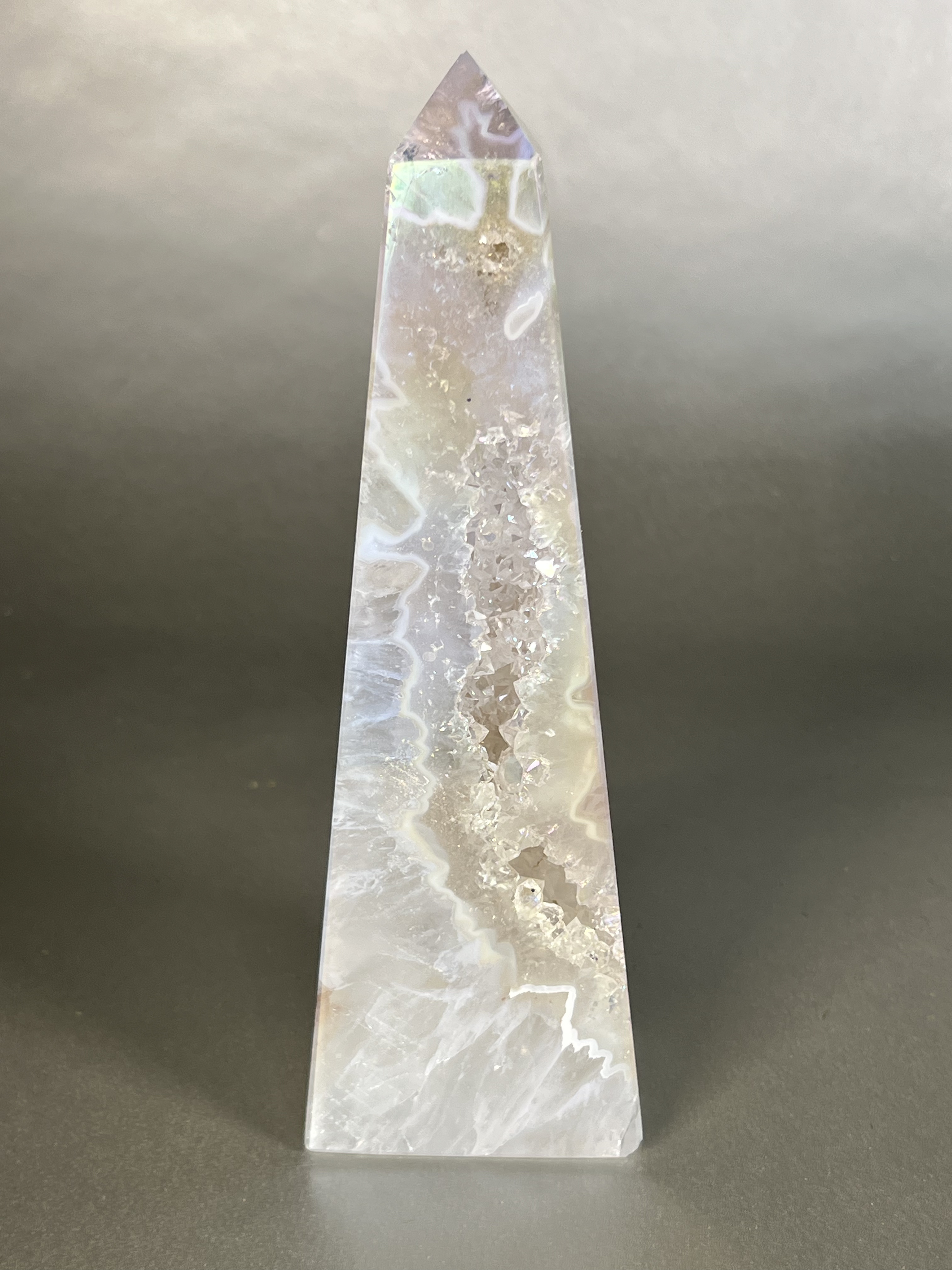 Experience the dreamy elegance of our Aura Agate Obelisk. Each one is uniquely crafted to exude a sense of luxury and exclusivity. Featuring the rare Aura Agate stone, this obelisk brings a touch of sophistication and beauty to any space. Elevate your decor with this truly one-of-a-kind piece. Approx. 2.5"x7" Aura Agate Tower