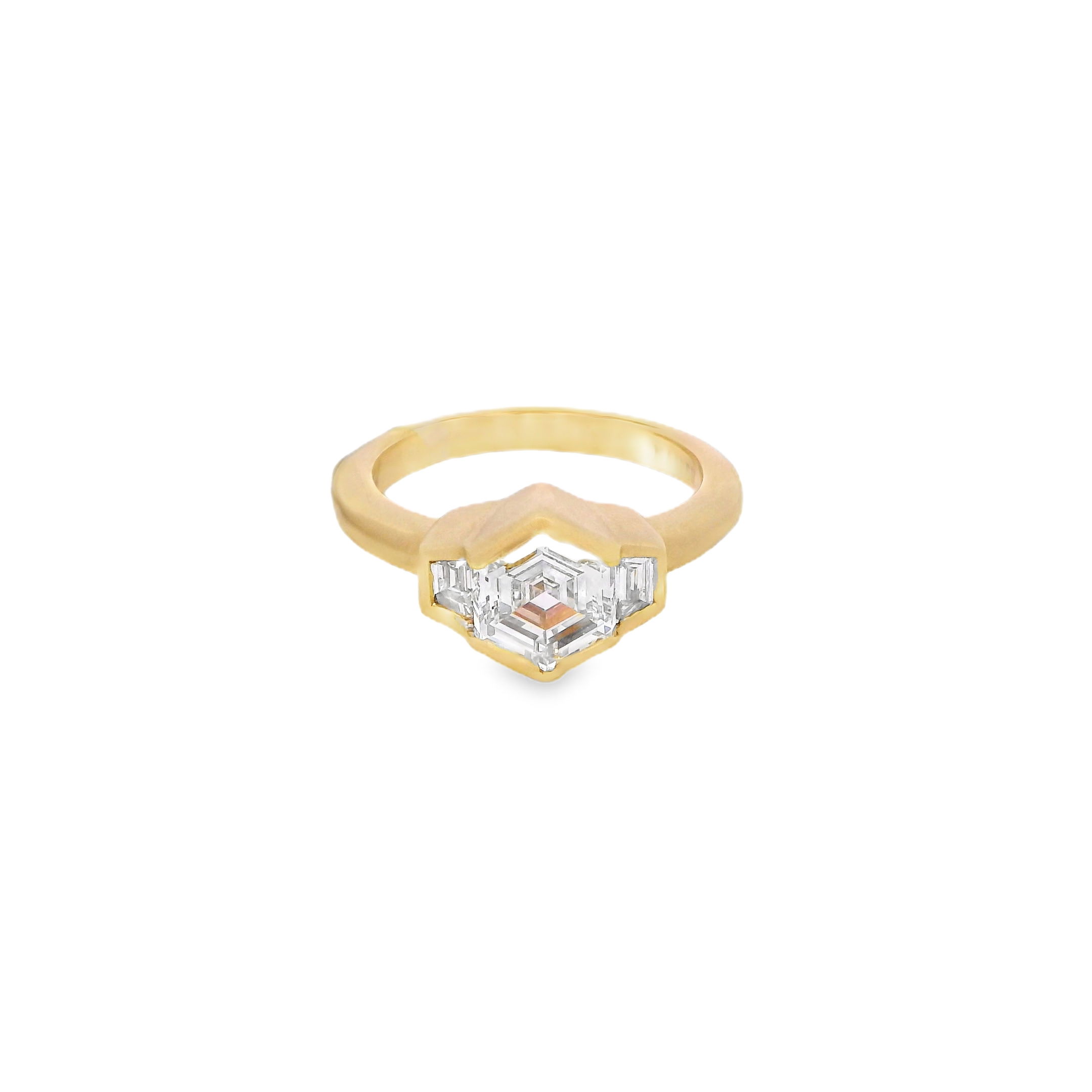 Modern elegance meets timeless symbolism in this stunning 18k Yellow gold three-stone ring. Featuring a unique hexagon-cut diamond set in a sleek bezel, this piece offers a contemporary twist on a classic design. The satin finish adds a soft, refined texture that highlights the geometric beauty of the center stone.-18k Yellow gold-Hexagon diamond, 1.51cts-Trapezoid diamonds, 0.16cts-Size 5.50, Contact for sizing optionsItem# 100-00938 Hexagon Three Stone Engagement Ring