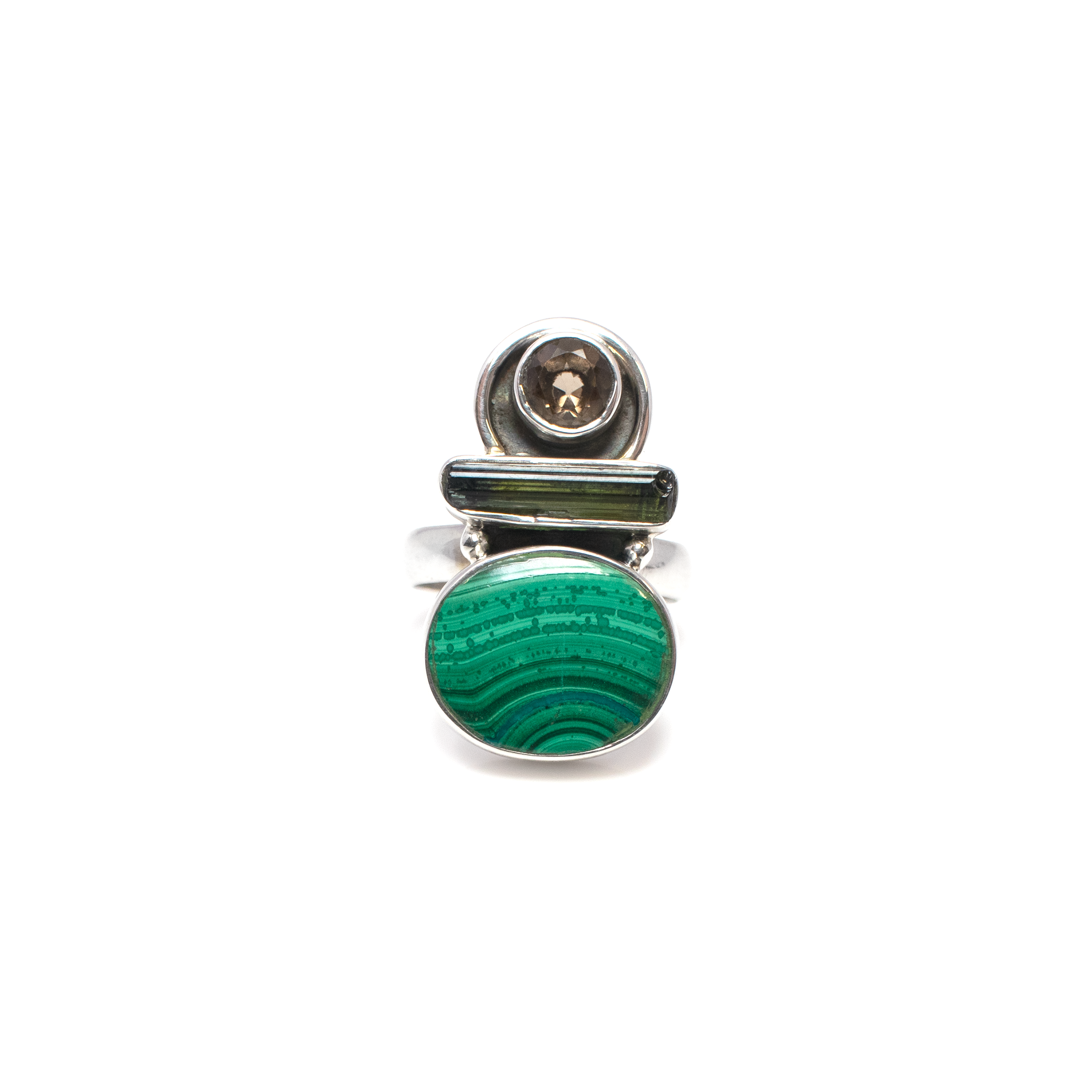 Elevate your jewelry collection with our exquisite Malachite Ring, a true masterpiece that embodies elegance and sophistication. Designed for those who appreciate the finer things in life, this ring is an impeccable blend of natural beauty and refined craftsmanship.At the heart of this captivating ring lies an oval-shaped malachite gemstone, renowned for its vibrant green hues and intricate, swirling patterns. Each stone is unique, ensuring your ring is truly one-of-a-kind.Flanking the malachite centerpiece are two dazzling green tourmaline gemstones. These exquisite accents not only enhance the overall beauty of the ring but also add a touch of luxury with their rich, vivid color.Completing the trio of gemstones are the subtle yet striking smoky quartz stones, which bring depth and a sophisticated contrast to the vibrant greens. Malachite Ring - Oval With Green Tourmaline & Smoky Quartz Sz7