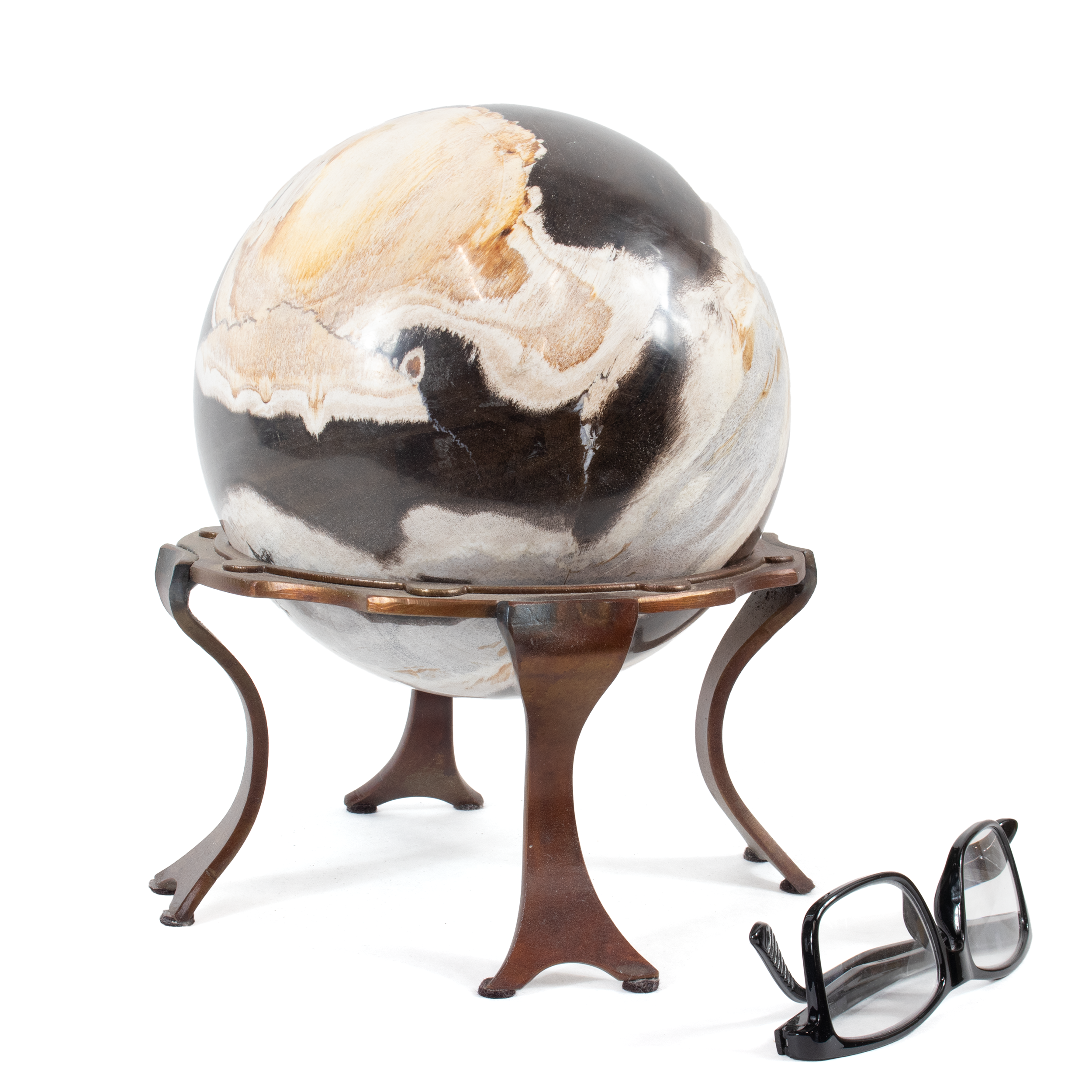 Elevate your home décor with the captivating allure of our Indonesian Petrified Wood Sphere, meticulously crafted to offer a touch of natural elegance and ancient history to any space. This stunning 6.5-inch sphere is a mesmerizing piece that seamlessly blends the timeless charm of petrified wood with modern design elements.Sourced from the lush, mineral-rich landscapes of Indonesia, this petrified wood sphere is a remarkable relic of ancient forests, showcasing intricate patterns and warm, earthy tones that have been transformed over millions of years. Paired with a sleek, custom copper ring stand, this piece adds a contemporary touch while providing a sturdy base. The warm glow of copper beautifully complements the rich hues of the petrified wood, creating a harmonious display. Indonesian Petrified Wood Sphere In Custom Ring Stand - 6.5 Inch Sphere In Copper