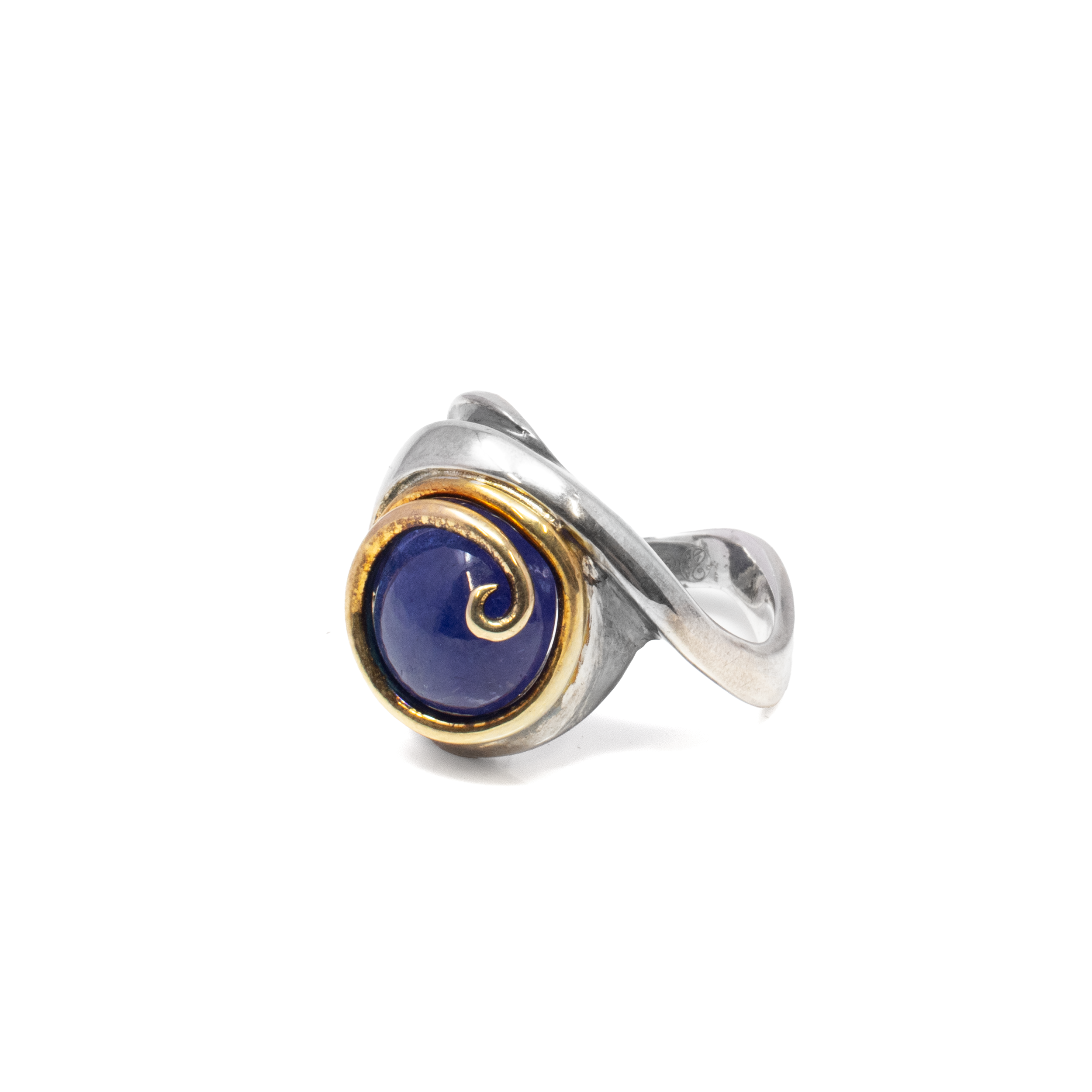 Immerse yourself in the mesmerizing allure of the Tanzanite Ring, a stunning piece of jewelry that beautifully encapsulates elegance and sophistication. At the heart of this exquisite ring lies a captivating round chatoyant cabochon tanzanite that shimmers with enchanting hues of deep blue and violet, reminiscent of a twilight sky.Expertly crafted for those who appreciate fine artistry, the tanzanite gemstone is securely nestled within an intricate gold vermeil bezel setting. The bezel is adorned with delicate swirl detailing, adding a touch of opulence and creating a timeless design that seamlessly mesmerizes from every angle. Tanzanite Ring - Round Chatoyant Cabochon With Gold Vermeil Swirl Detailed Bezel Set On Twisted Sterling Silver Band Sz9