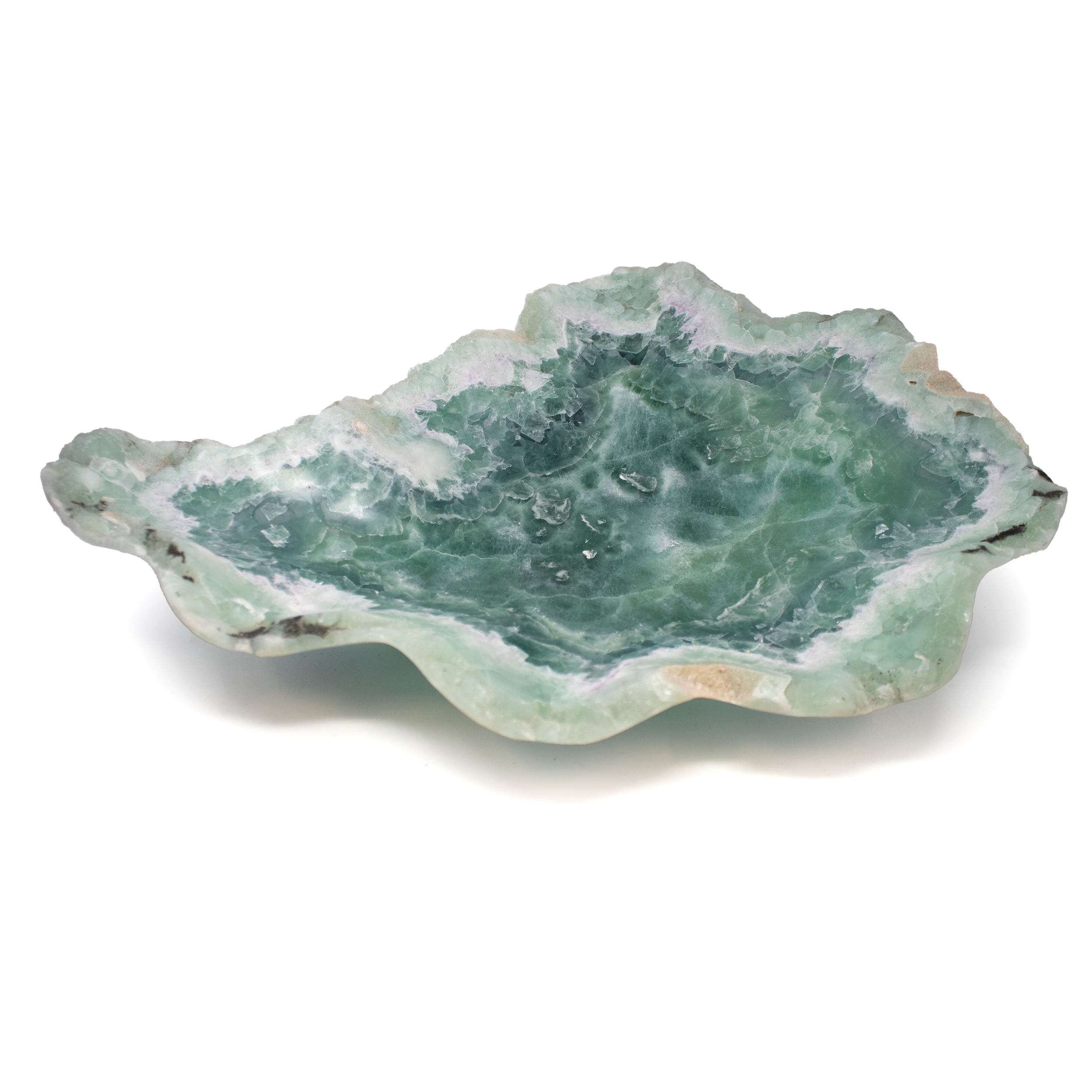 Fluorite Onyx Vessel – Shallow Depth, a handcrafted bowl carved in Mexico from high-quality fluorite onyx. This striking piece features a marbled blend of green, purple, and creamy white tones, with fluid banding that captures the natural elegance of the stone. The shallow profile enhances its versatility, making it ideal as a centerpiece, catchall, or serving bowl for dry goods.Polished to a luminous finish, each vessel is one-of-a-kind, with unique color transitions and organic patterning that add a refined, sculptural touch to any interior. Whether styled on a coffee table, entryway console, or dining surface, this gemstone bowl brings harmony and visual interest to modern and eclectic spaces alike. A timeless addition for collectors of natural decor and functional art. Fluorite Onyx Vessel - Shallow Depth - from Mexico