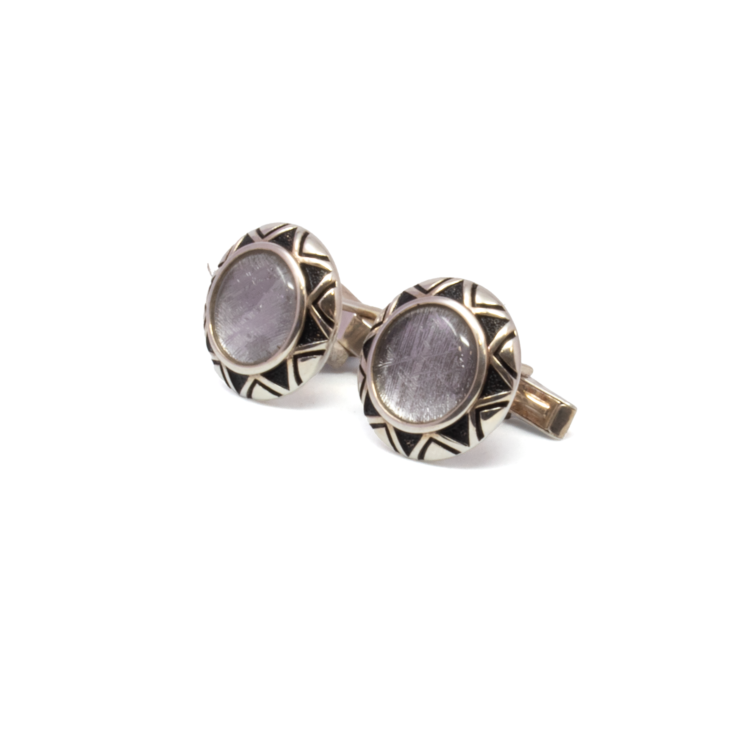 Elevate your style with these extraordinary Muonionalusta Meteorite Cufflinks, featuring a bold round design that fuses cosmic wonder with artisan detail. Genuine slices of the 4.5-billion-year-old Muonionalusta meteorite reveal intricate Widmanstätten patterns, framed in polished 925 sterling silver bezels engraved with tribal motifs that echo the mystery of the stars. A discreet crystal accent adds a refined glint, balancing the raw, metallic beauty with modern elegance. Perfect for collectors, dreamers, or those who seek meaning in their accessories, these cufflinks offer a rare blend of deep history and contemporary sophistication. Muonionalusta Meteorite Cufflinks - Round With Crystal And Tribal Bezel