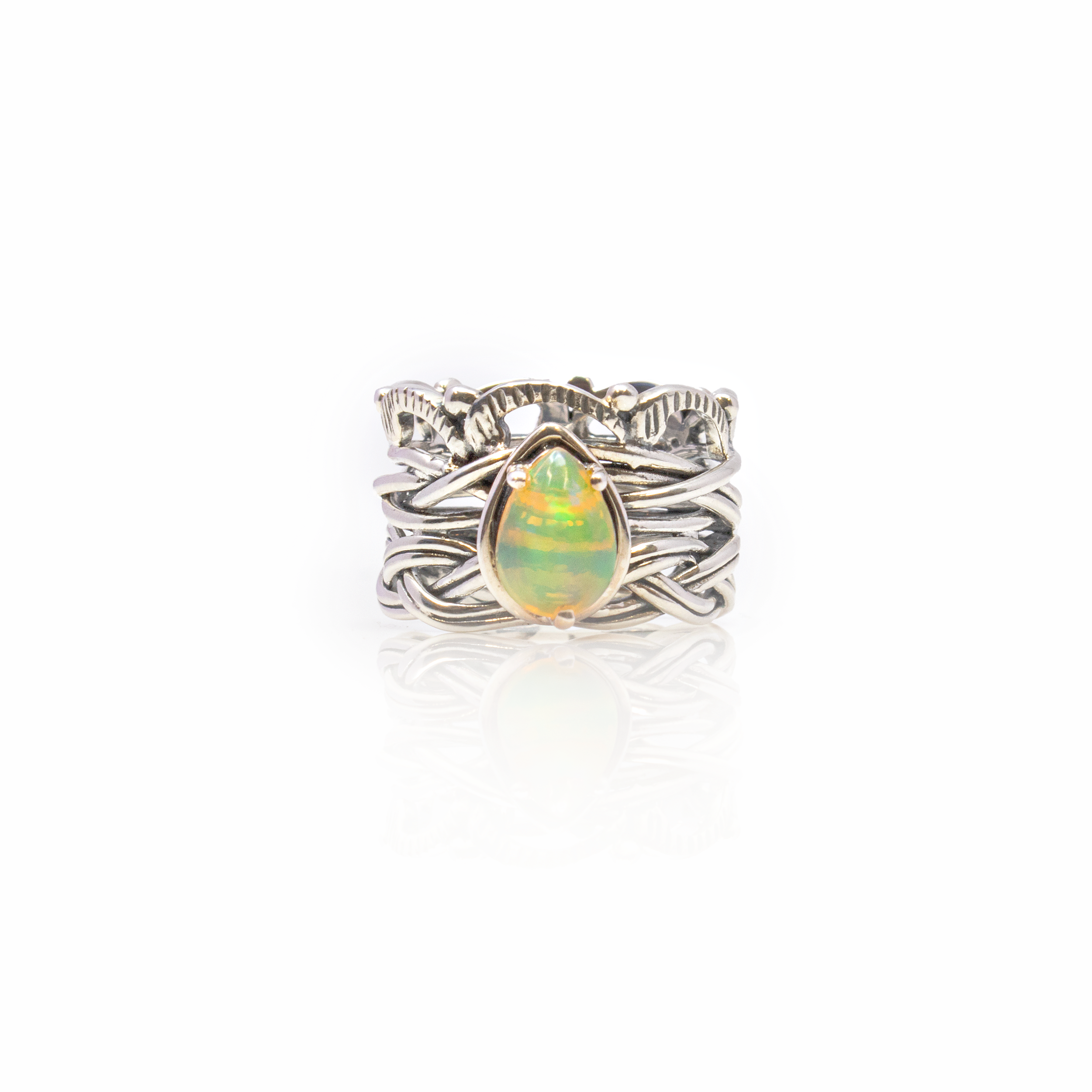 Elevate your jewelry collection with this exquisite Ethiopian Opal Ring, a true masterpiece that captures the luminous beauty of this unique gemstone. At the heart of this stunning piece is a brilliantly colored pear-shaped cabochon Ethiopian Opal. Its mesmerizing play-of-color flashes with a spectrum of fiery colors, reminiscent of a magical dance of light and shadow. This opulent gem is securely prong-set within a high-quality 925 sterling silver bezel, ensuring both durability and elegance. The bezel is meticulously crafted, featuring an intricate braided and vine design that gracefully wraps around the band. This delicate embellishment adds an organic and timeless touch, enhancing the natural beauty of the opal. Ethiopian Opal Ring - Pear Cabochon Prong Set On 925 Sterling Silver Bezel With Braided & Vine Design Sz9