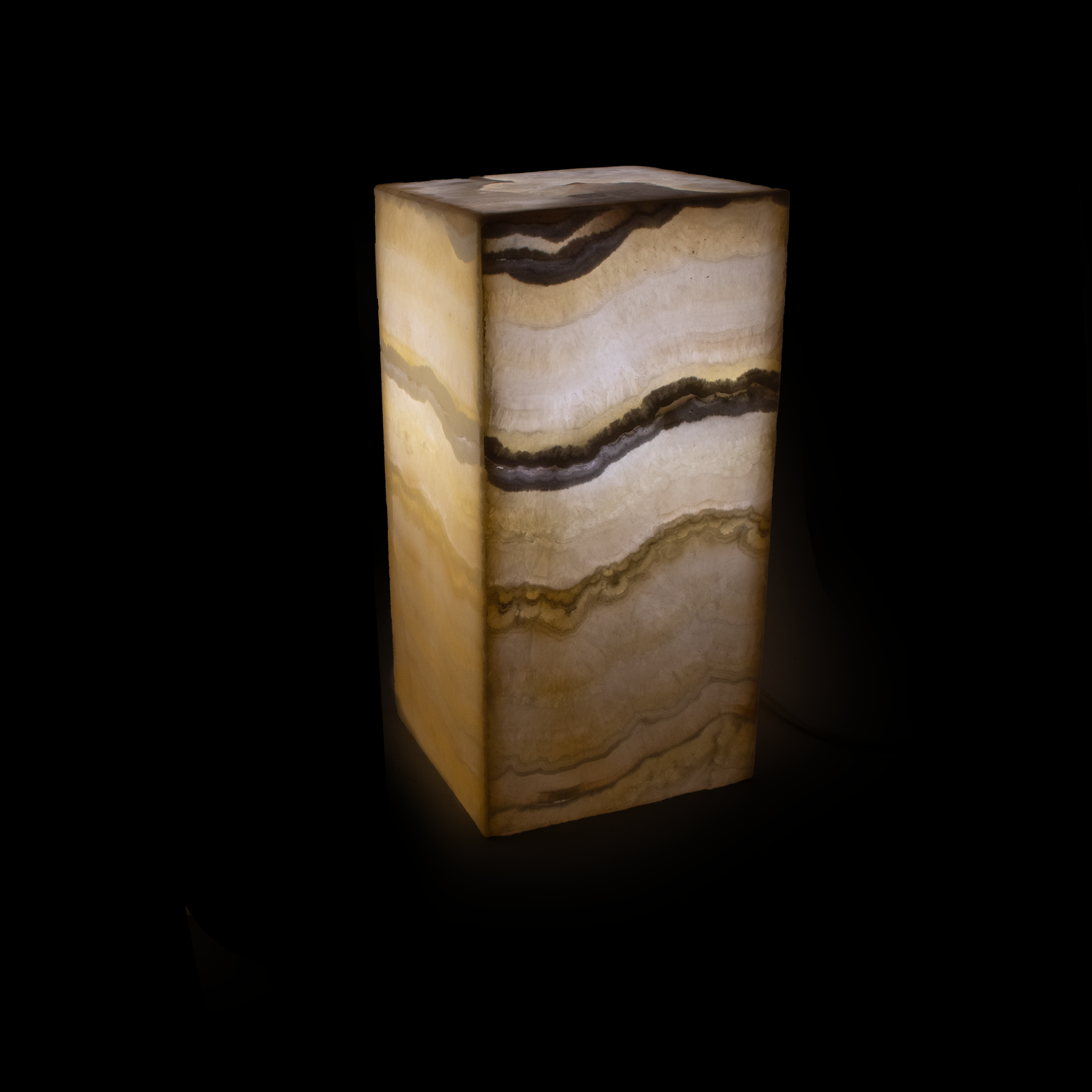 Introducing the Nube Square Onyx Luminary Pedestal – a mesmerizing fusion of art and functionality that elevates any space with its radiant charm. Crafted from exquisite Mexican Onyx, this table lamp showcases the natural beauty and unique character of the stone, casting a warm, inviting glow that transforms any room into an oasis of tranquility.The Nube Square Onyx Luminary Pedestal stands as a testament to superior craftsmanship and timeless design. Its bold, square silhouette adds a touch of modern sophistication, seamlessly complementing a variety of interior styles, from contemporary to classic. Each lamp is a one-of-a-kind masterpiece, featuring distinctive veining and variations inherent to the onyx stone, ensuring that your luminary is as unique as your personal style. Nube Square Onyx Luminary Pedestal