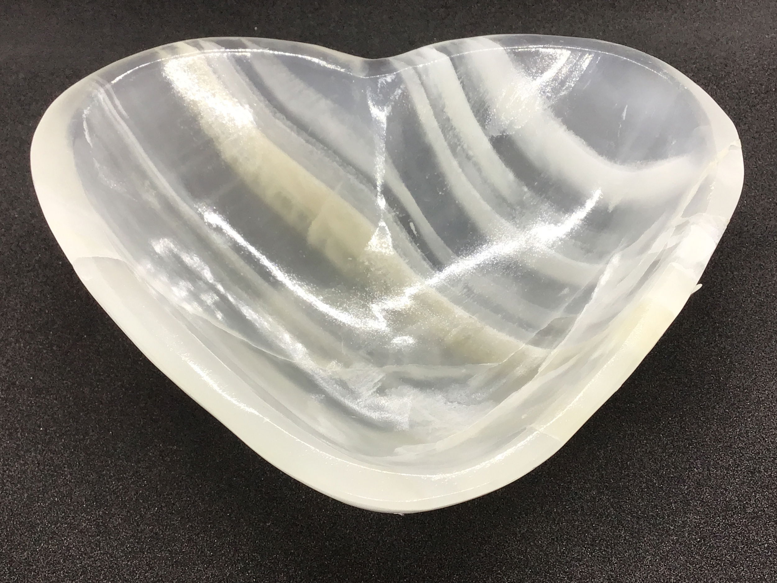 Introducing the exquisite Ice White Onyx Heart Vessel—an enchanting masterpiece crafted from genuine Mexican Onyx. This mesmerizing heart-shaped vessel is not only a stunning decorative piece but also a symbol of elegance and tranquility.Onyx is not only celebrated for its visual appeal but also revered for its purported healing properties, believed to help balance emotions and promote clarity. The cool, tranquil appearance of Ice White Onyx introduces a serene ambiance to your space, harmonizing beautifully with any interior design style.- Home and office decor enthusiasts seeking a touch of elegance and natural artistry.- Gift-givers looking for a meaningful and unique present for special occasions like anniversaries, weddings, or Valentine's Day.- Collectors of fine minerals and those who appreciate the nuanced variations and vibrancy that natural onyx provides.Elevate your space with the Ice White Onyx Heart Vessel—a timeless treasure that blends the wonder of nature with refined artistry. Ice White Onyx Heart Vessel