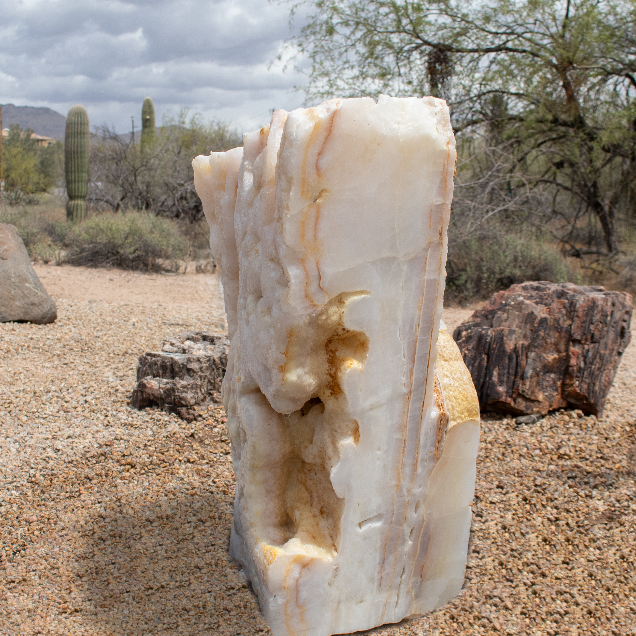This White Onyx Fountain boasts a distinctive design with two contrasting sides—a smooth, cut side that highlights the elegant veining of the onyx, and a bubbly side that enhances the soothing, natural aesthetic. The combination of textures creates a dynamic visual appeal that is both modern and timeless. Enhance the tranquil ambiance with carefully selected fountain rocks that complement the onyx’s natural tones. This White Onyx Fountain brings a touch of nature’s artistry to any location. It’s perfect for creating a serene atmosphere in a living room, patio, or courtyard. Paired with the gentle sound of flowing water, it transforms any space into an oasis of relaxation and style. Let Rare Earth Gallery’s white-glove service make your fountain dreams come true—simply choose your fountain, tell us where it goes, and we’ll handle the rest, from delivery to installation. IMPORTANT: the purchase price listed is for the FOUNTAIN ONLY and DOES NOT INCLUDE the cost of a basin, pump, parts or installation. Before purchasing a fountain online, we STRONGLY recommend you call us at (480) 575-4360 for a FREE consultation to discuss these additional costs and schedule a pre-site inspection. Also, free shipping does NOT apply to fountains, please call for a quote. White Onyx Fountain with Cut Side and Bubbly Side with Set Pin Plate