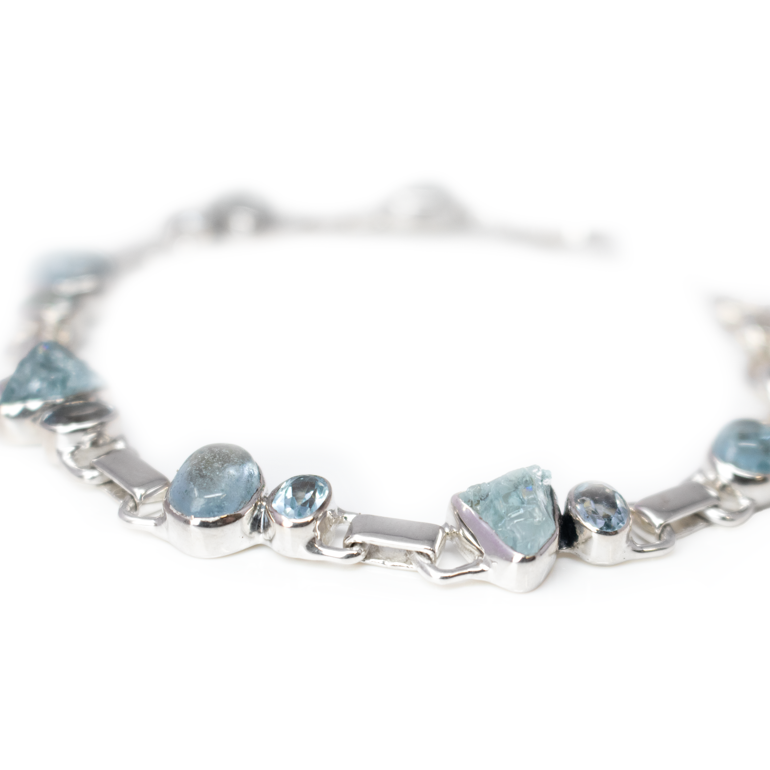 Introducing the Aquamarine Link Bracelet, a stunning embodiment of oceanic elegance and artisanal craftsmanship. This exquisite piece is designed to captivate with its rich hues and luxurious materials, making it a perfect addition to any jewelry collection.Adorn your wrist with the natural beauty of rough nugget aquamarines, each uniquely formed by nature and exuding a raw, organic charm. The enchanting glow of the oval cabochon aquamarines is perfectly complemented by the sparkling brilliance of faceted blue topaz ovals. Together, these gemstones create a harmonious ballet of soothing blues and radiant brilliance, invoking the serene beauty of a tranquil sea. Aquamarine Link Bracelet - Rough Nuggets & Oval Cabochons with Faceted Blue Topaz Ovals - 925 Sterling Silver Bezels & Links