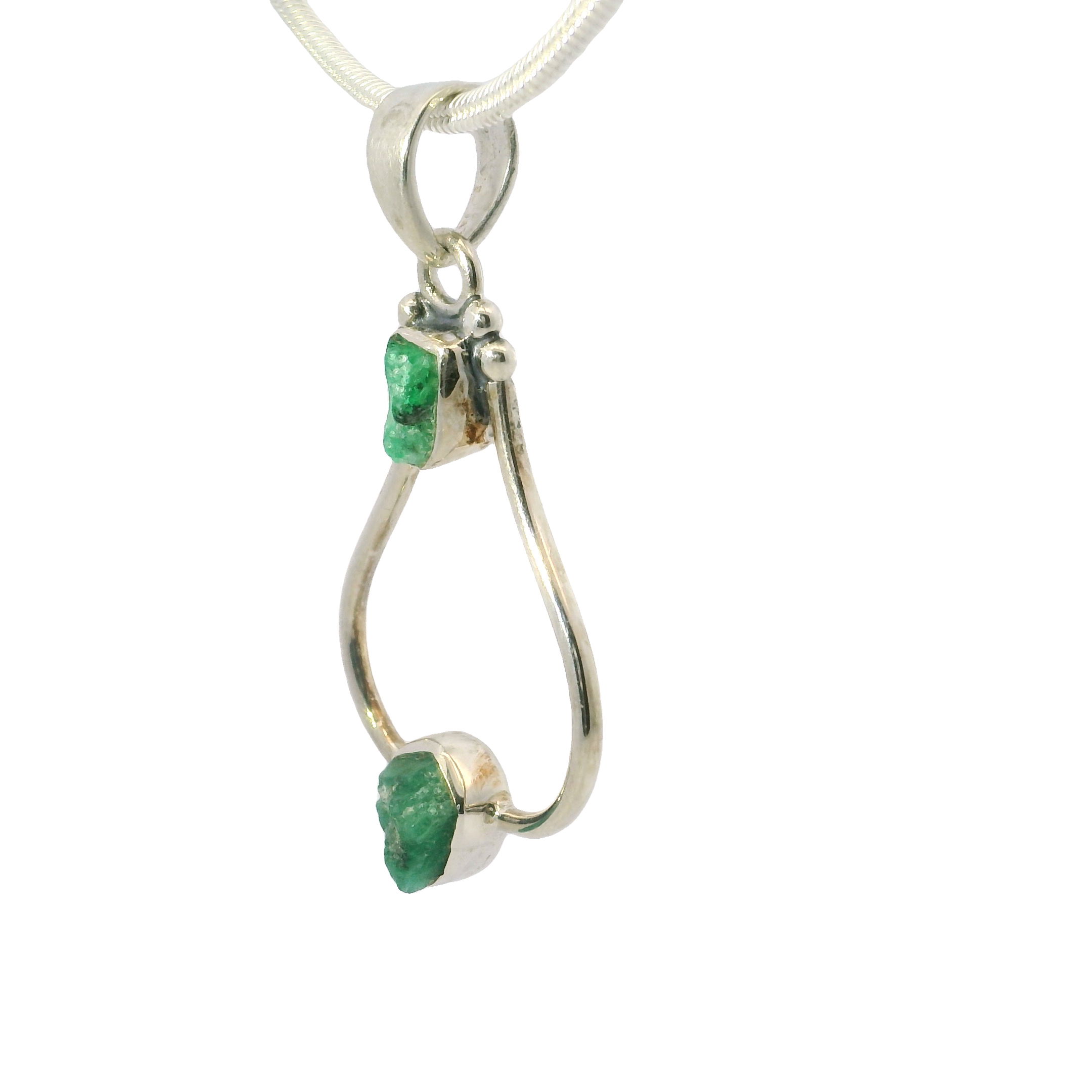 Discover elegance redefined with our enchanting Emerald Pendant, featuring two raw yet captivating rough freeform emeralds set in an open design. Each emerald is carefully encased in a 925 sterling silver bezel, accentuating the natural beauty and vibrant green hue of the gemstones. The open silver setting not only highlights the organic forms of the emeralds but also allows light to dance around them, creating a mesmerizing play of color and sparkle.This unique piece is perfect for those who appreciate the harmonious blend of nature’s spontaneity and refined craftsmanship. Whether worn as a statement piece or cherished addition to your gemstone collection, this pendant embodies timeless sophistication and style. The durable 925 sterling silver ensures longevity, while its hypoallergenic properties make it suitable for all-day wear. Emerald Pendant - 2 Rough Freeforms with 925 Sterling Silver Bezels on Open Silver Setting