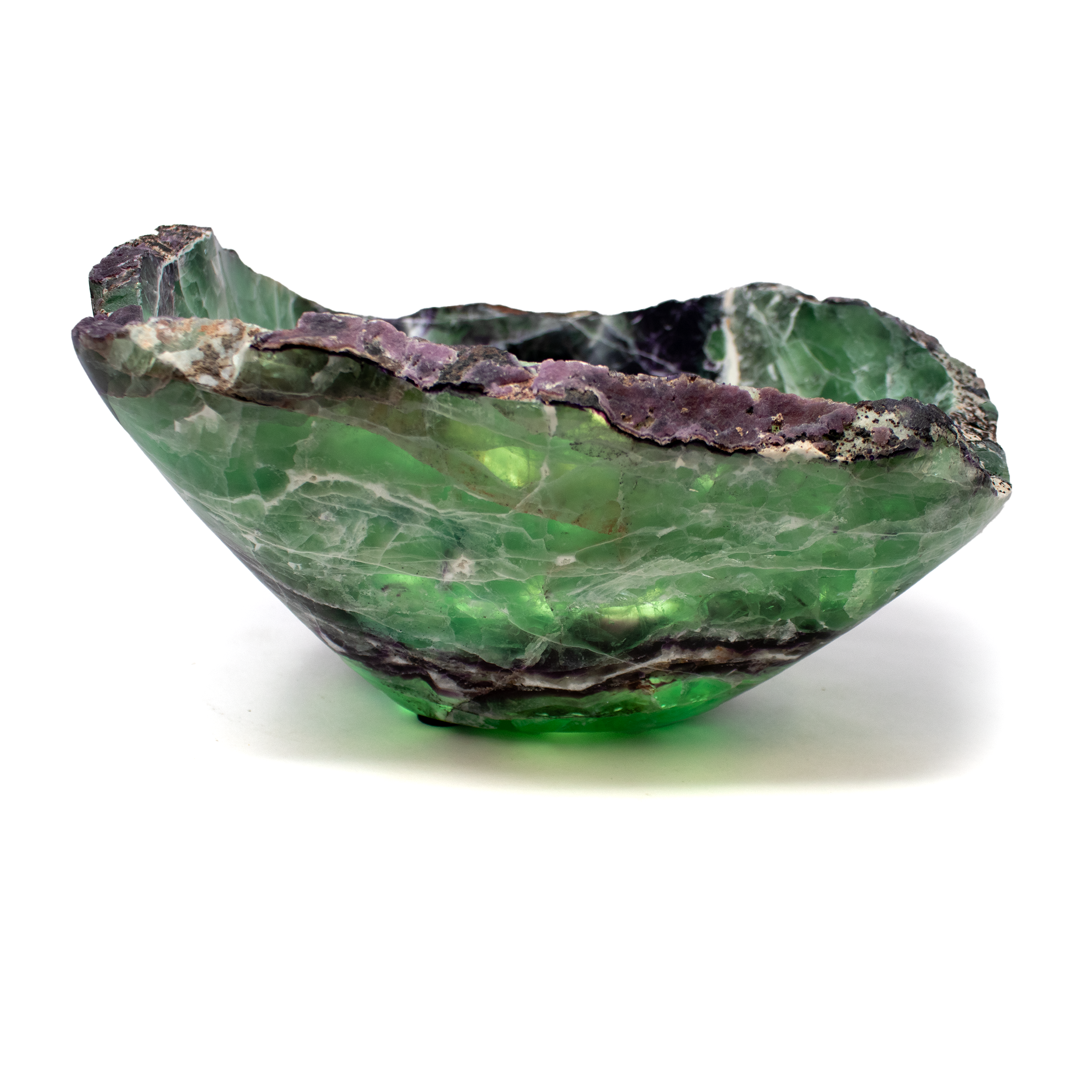 A+ Fluorite Vessel with Natural Edge, a sculptural bowl carved in Mexico from premium-grade fluorite. This extraordinary piece showcases a vivid interplay of purples, greens, and soft blues, with translucent layers that reveal the mineral’s natural complexity. The preserved raw edge lends an organic, elemental contour that contrasts beautifully with the polished inner surface.Each vessel is one-of-a-kind, with distinct banding and coloration that reflect the unique formation of the stone. Ideal as a tabletop centerpiece, decorative catchall, or standalone work of art, this fluorite bowl brings a touch of natural elegance to any space. A refined addition for collectors of mineral decor or those seeking meaningful, earth-sourced interior accents. A+ Fluorite Vessel With Natural Edge From Mexico
