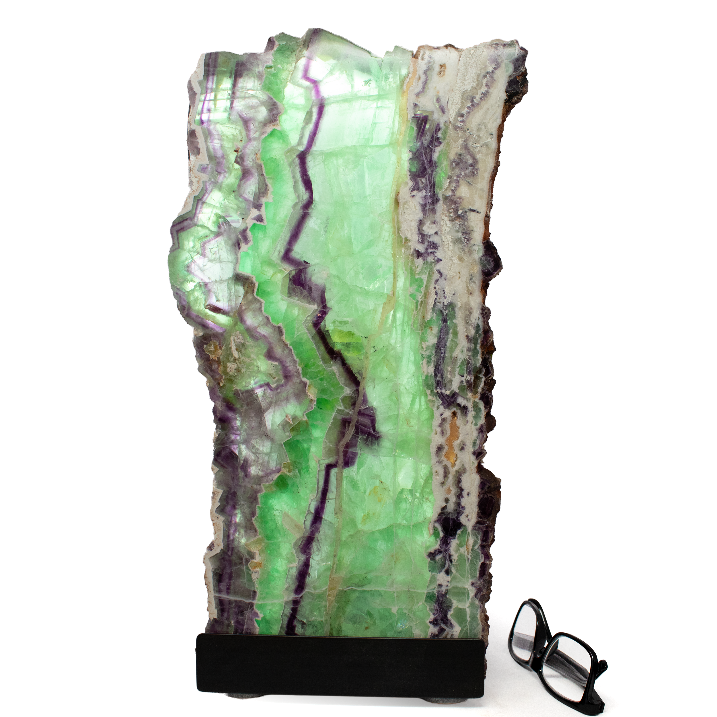 Illuminate your space with the enchanting glow of our Rainbow Fluorite Table Lamp - Slice Set Vertical with Natural Live Edge. Perfectly combining the beauty of nature with functional home decor, this stunning luminary showcases exquisite slices of rainbow fluorite, renowned for its captivating colors and unique patterns. Each lamp is a one-of-a-kind masterpiece, boasting a natural live edge that highlights the raw and organic beauty of the fluorite. The vertical arrangement of the slices creates a mesmerizing display of vibrant hues, ranging from deep purples and blues to rich greens and yellows, each one telling its own story. Rainbow Fluorite Table Lamp - Slice Set Vertical with Natural Live Edge