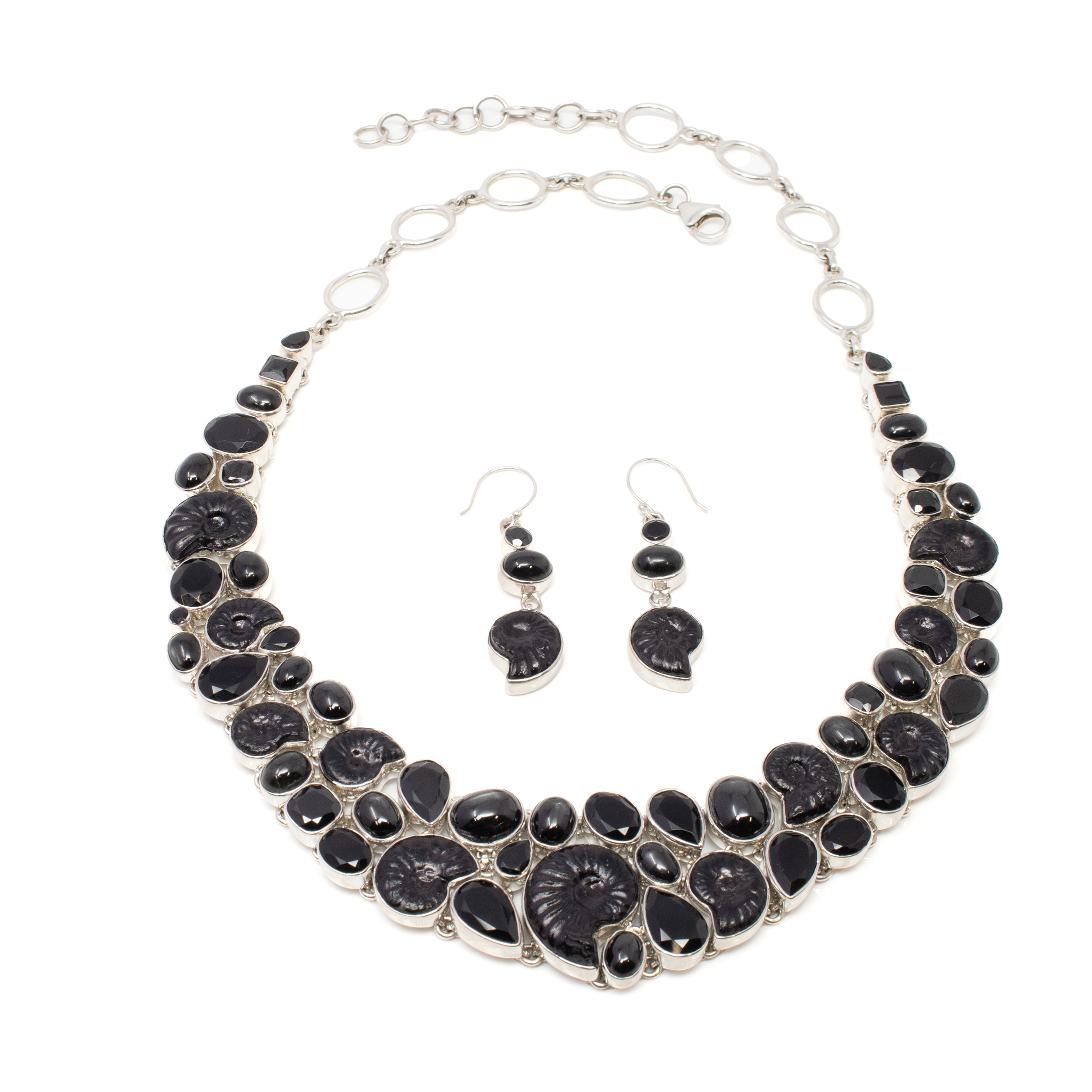 Introducing the captivating Black Ammonite Set, a stunning fusion of nature's timeless beauty and luxurious elegance. This exquisite jewelry set features a necklace and a pair of dangle earrings, meticulously crafted to enhance your style with a touch of mystique.The centerpiece of this set is the enchanting ammonite fossil, renowned for its naturally intricate spiral pattern. The ammonites are beautifully complemented by faceted black onyx stones, which reflect light with every movement, adding a dazzling effect to your outfit. Nestled alongside the onyx are black star garnet cabochons, each displaying a mesmerizing asterism, reminiscent of a starry night.The necklace gracefully drapes around the neck, showcasing the unique interplay of textures and tones. Its adjustable chain ensures a comfortable fit for any occasion, whether you are attending a formal event or adding flair to your everyday look.The dangle earrings, designed to gently sway with each turn of the head, perfectly mirror the elegance of the necklace. Black Ammonite Set - Necklace & Dangles Earrings with Faceted Black Onyx & Black Star Garnet Cabochons
