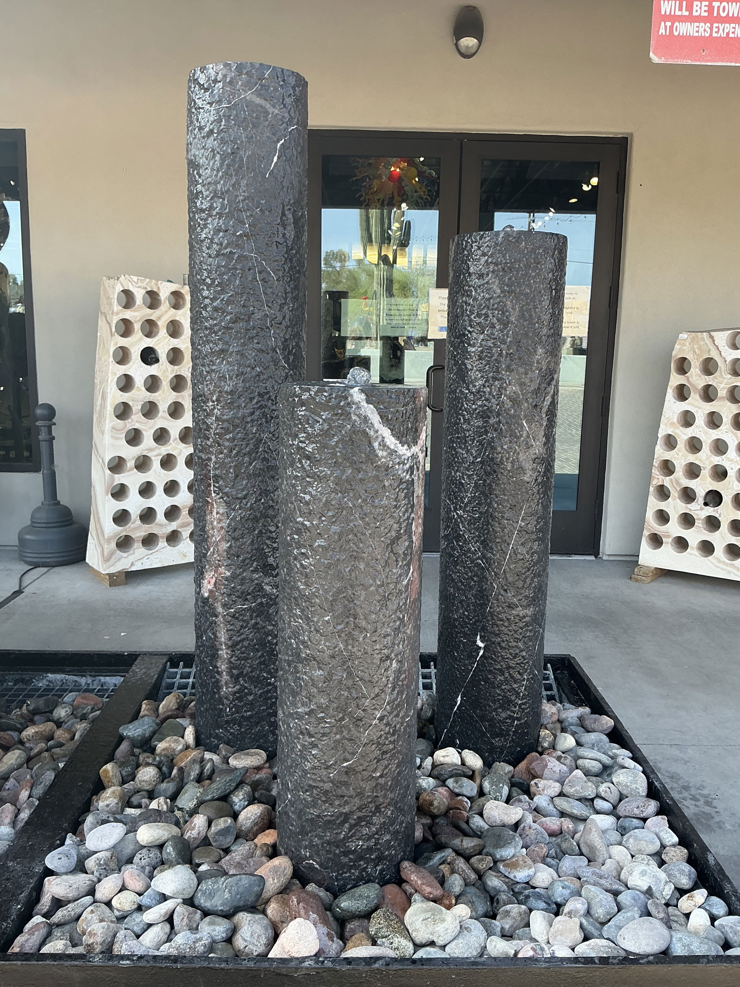 This exquisite fountain set features three sleek cylindrical fountains, expertly crafted from premium black marble, renowned for its durability and luxurious appearance. Each cylinder in the Trio varies in height, creating a visually dynamic display that enhances the natural beauty of marble's intricate veining and rich, deep color. The textured surfaces reflect light beautifully, creating a mesmerizing play of reflections and shadows, while the gentle cascade of water from the top of each cylinder produces a calming, meditative ambiance. Let Rare Earth Gallery’s white-glove service make your fountain dreams come true—simply choose your fountain, tell us where it goes, and we’ll handle the rest, from delivery to installation. IMPORTANT: the purchase price listed is for the FOUNTAIN ONLY and DOES NOT INCLUDE the cost of a basin, pump, parts or installation. Before purchasing a fountain online, we STRONGLY recommend you call us at (480) 575-4360 for a FREE consultation to discuss these additional costs and schedule a pre-site inspection. Also, free shipping does NOT apply to fountains, please call for a quote. Black Marble Cylinder Fountain TRIO SET