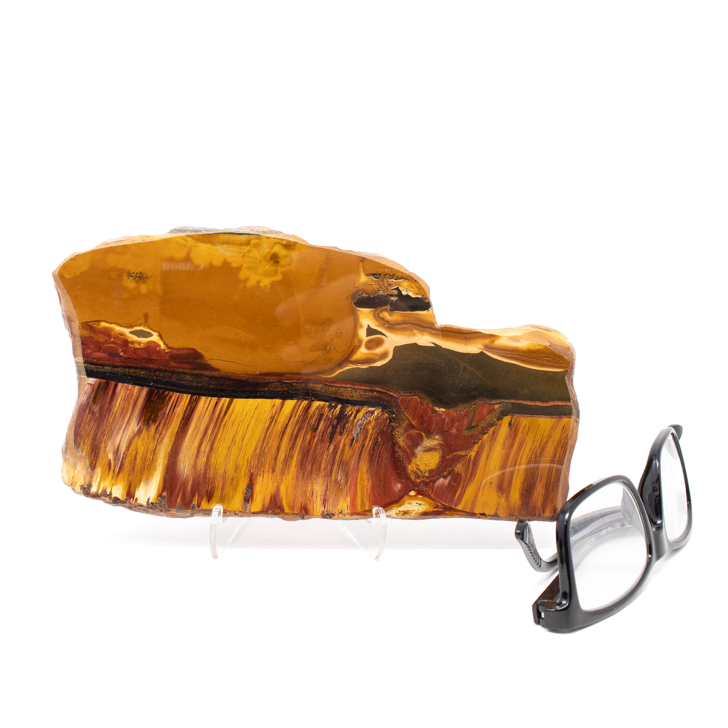 Discover the exquisite beauty and captivating allure of the Mara Mamba Tiger Eye Slice, an enchanting addition to any crystal or mineral collection. Sourced from the ancient lands of Australia, this freeform slice showcases the mesmerizing interplay of vibrant colors and unique patterns that Mara Mamba Tiger Eye is renowned for. Our Mara Mamba Tiger Eye Slice boasts a stunning combination of rich golden, and deep red hues, brought to life by nature's artistry over millions of years. Each piece is hand-selected for its unique characteristics and striking appearance. Unlike mass-produced stones, this freeform slice retains its organic shape, enhancing its natural beauty and individuality. The unpredictable bands and shimmering chatoyancy of the Tiger Eye create a dynamic visual experience that changes with every glance. Mara Mamba Tiger Eye Slice - Freeform with Lucite Easel from Australia