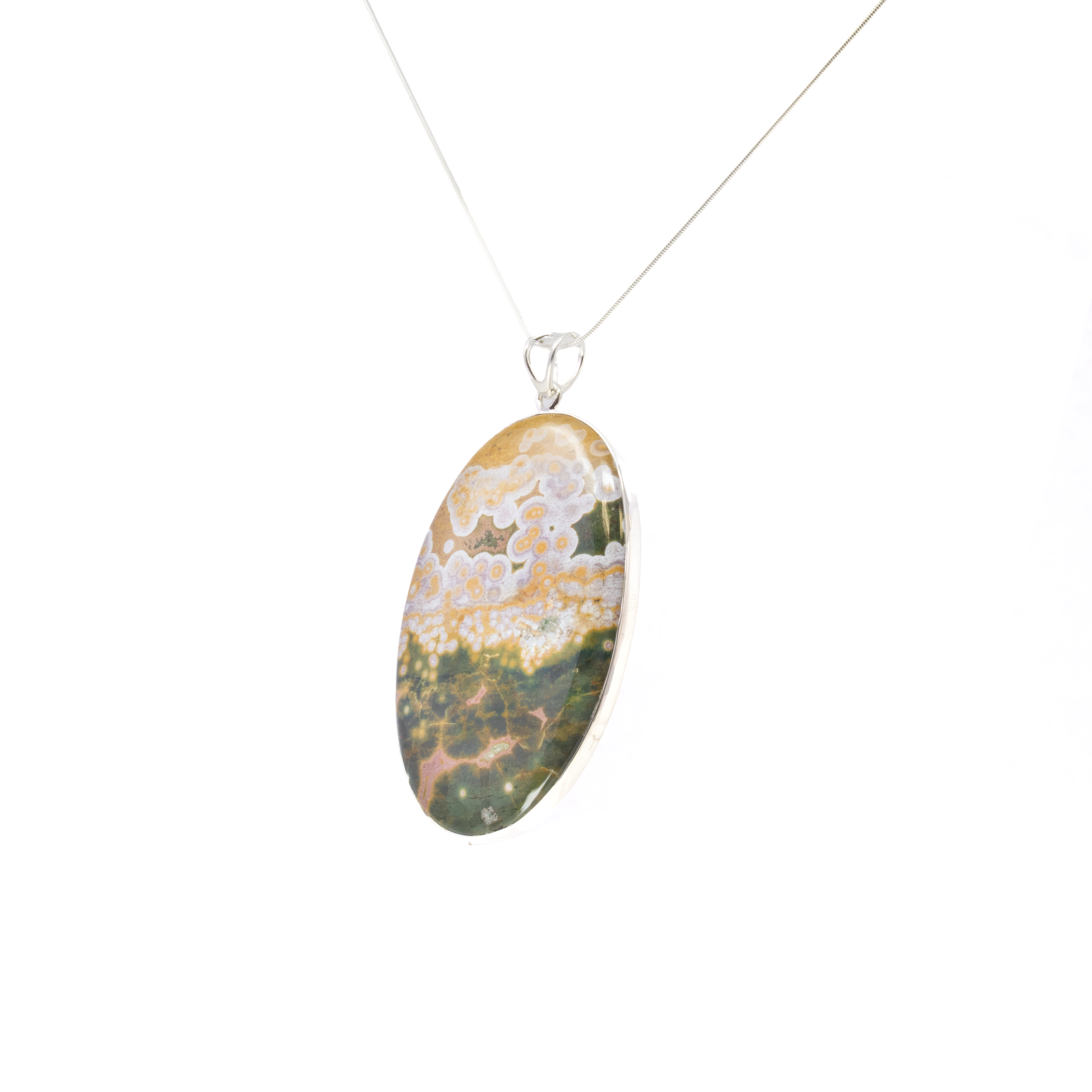 Introducing our Ocean Jasper Pendant, a captivating statement piece that embodies the unique beauty of nature. This exquisite pendant features a large oval cabochon of ocean jasper, renowned for its mesmerizing patterns and rich coloration. Housed in a simple yet elegant 925 sterling silver bezel, the pendant highlights the stone’s deep green hues, accented by striking golden ochre orbicular formations and delicate pink veining. With a substantial size of over three inches, this pendant is perfect for women who appreciate bold, artistic expressions in their jewelry. Each ocean jasper stone is one-of-a-kind, ensuring that your pendant is a true original. The calming green tones and intriguing patterns make it a versatile accessory, suitable for both casual and formal occasions. Ocean Jasper Pendant - Large Oval Cabochon with Simple 925 Sterling Silver Bezel & Deep Green Hues with Golden Ochre Orbiculars & Pink Veining 3"+