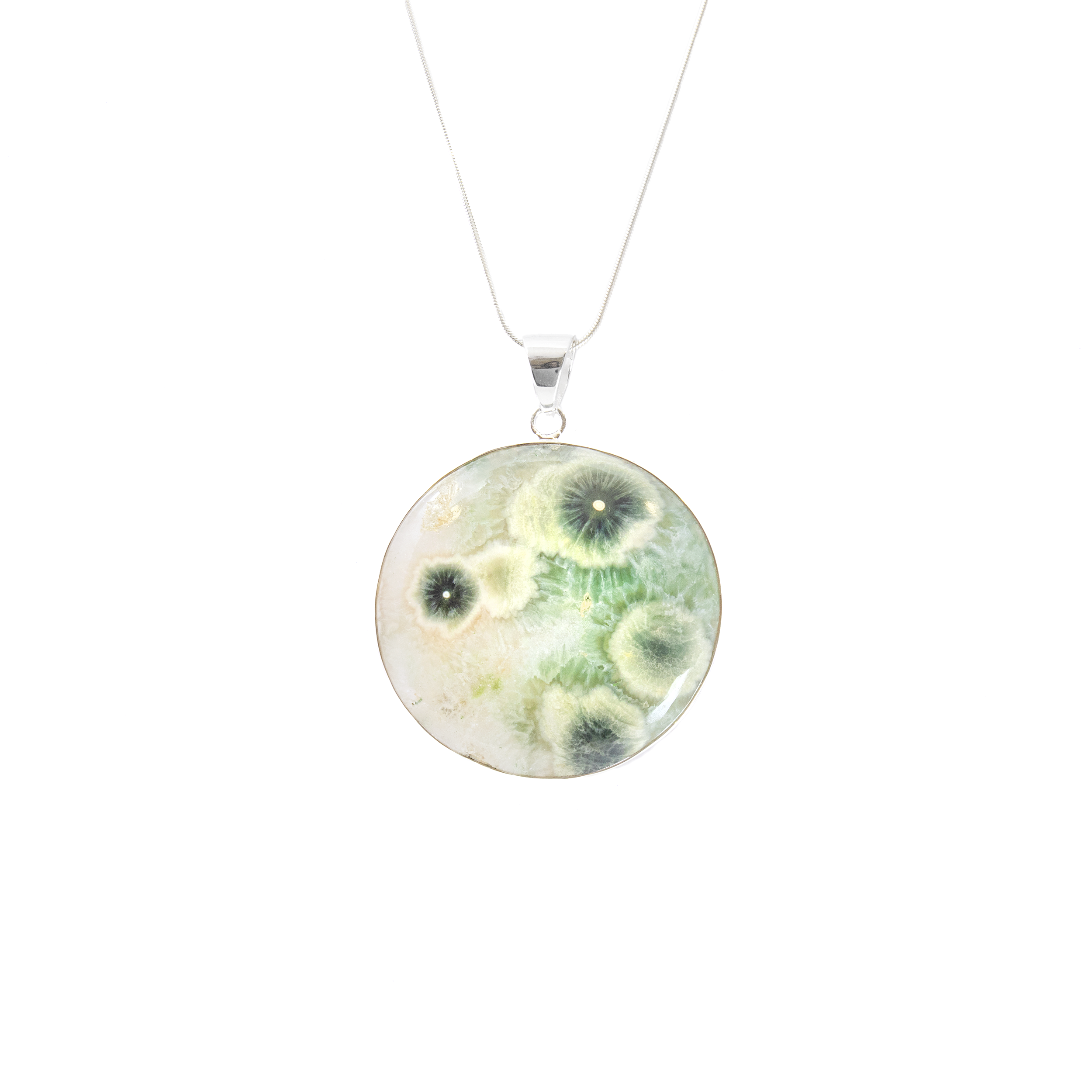 Elevate your jewelry collection with this exquisite Ocean Jasper Pendant, a true testament to nature's artistry. Carefully crafted for women who appreciate the unique beauty and elegance of gemstone jewelry, this pendant is perfect for any occasion.This striking pendant showcases a round cabochon of genuine Ocean Jasper, renowned for its captivating patterns and vibrant colors. At its heart, the pendant features dramatic green flower bursts, skillfully highlighted with sage green edges. Each stone's natural variations ensure that your pendant is a one-of-a-kind masterpiece.The Ocean Jasper Pendant is more than just a piece of jewelry—it's a connection to the earth's wonders. Its soothing green tones and nature-inspired patterns bring a sense of peace and tranquility, making it a thoughtful gift for someone special or a cherished addition to your personal collection. Ocean Jasper Pendant - Round Cabochon with Simple 925 Sterling Silver Bezel & Vibrant Green Flower Bursts with Sage Green Edges 2"