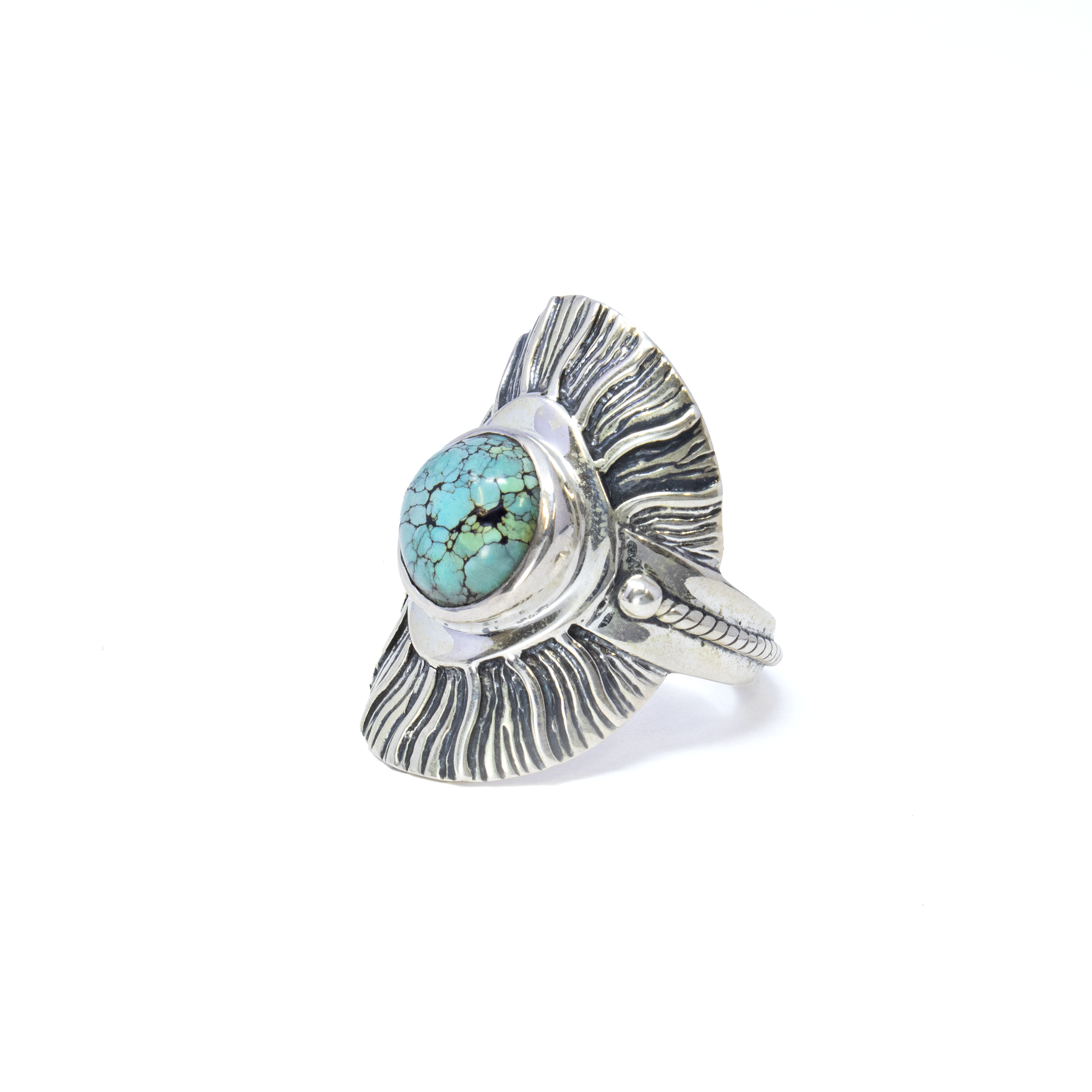 Discover the enchanting beauty of our Turquoise Ring from Tibet, a captivating piece that effortlessly blends tradition with elegance. This exquisite ring features a striking round cabochon of genuine turquoise, renowned for its vibrant hues and natural patterns, each telling its own unique story. The cabochon is meticulously set into a 925 sterling silver bezel, ensuring both durability and timeless charm.Enhancing the allure of the turquoise, the bezel is adorned with a sun ray design edge that adds a radiant and sophisticated touch, capturing the light beautifully with every movement. The attention to detail continues with the artisanal rope accent along the band, providing a perfect contrast to the polished silver, and adding a layer of texture to the overall design. Turquoise Ring from Tibet - Round Cabochon Set on 925 Sterling Silver Bezel with Sun Ray Design Edge & Rope Accent on Band sz10