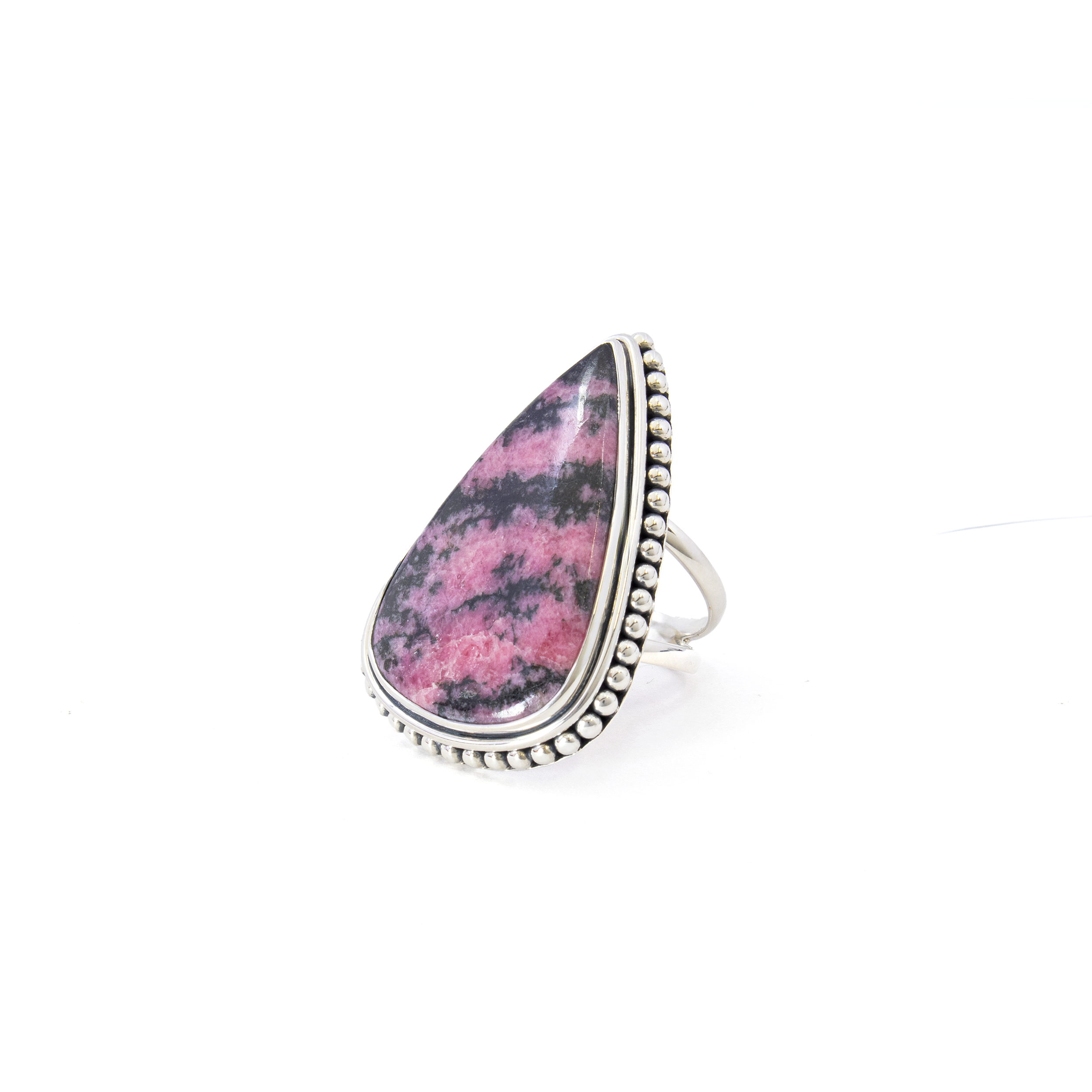 Introducing our exquisite Rhodonite Ring, a stunning piece of jewelry that effortlessly combines elegance and craftsmanship. This beautiful ring features a captivating pear-shaped cabochon made from genuine rhodonite, known for its soothing pink hue interspersed with alluring black veins. The cabochon is expertly set in a 925 sterling silver bezel, ensuring a secure fit while enhancing its natural beauty.The bezel is adorned with a delicate beaded edge, adding a touch of sophistication and contemporary flair to the design. This attention to detail is further complemented by the ring's unique double band, providing both durability and a modern aesthetic, making it a perfect statement piece for any occasion. Rhodonite Ring - Pear Cabochon with 925 Sterling Silver Bezel & Beaded Edge on Double Band sz10