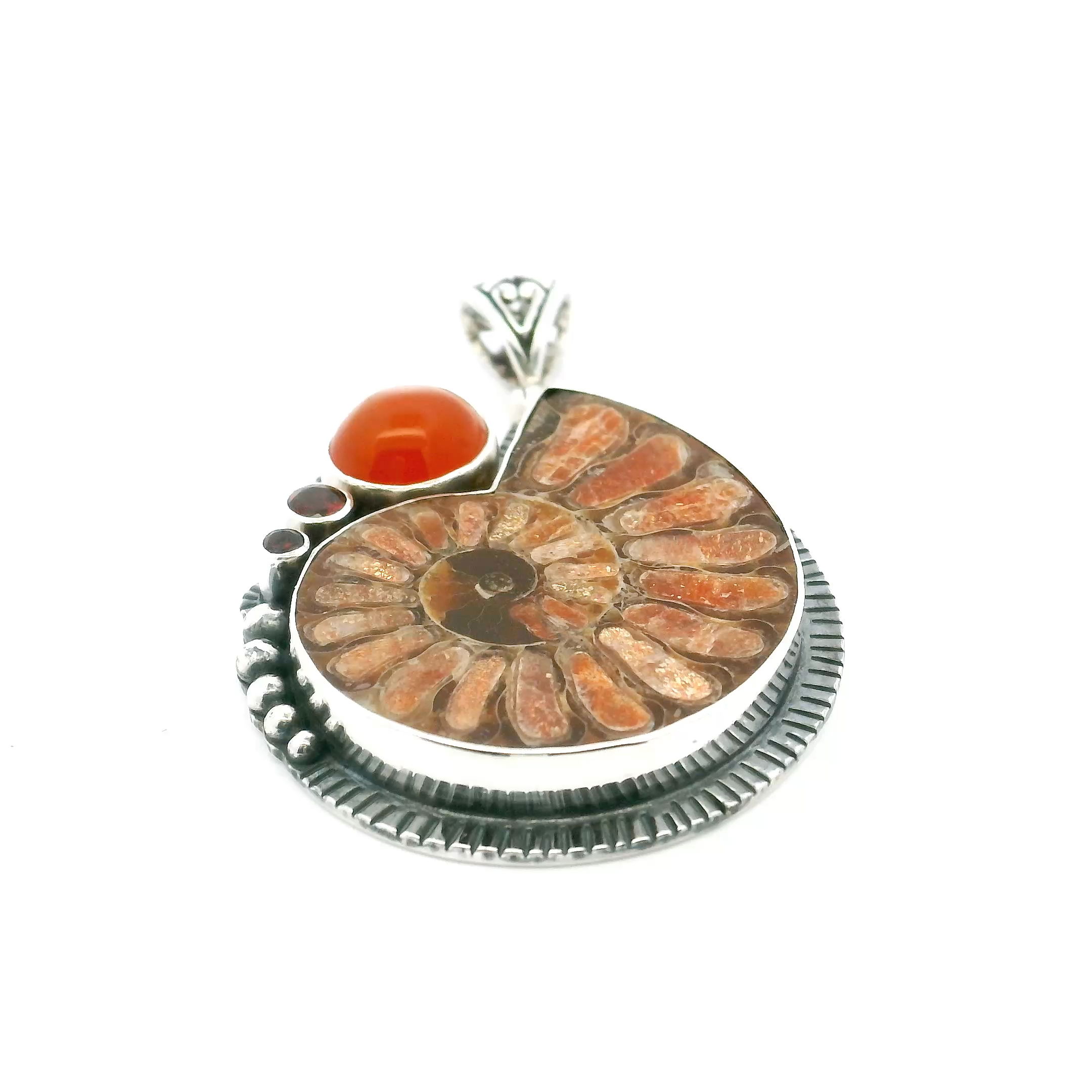 Add timeless elegance to your collection with our Ammonite Fossil Pendant. Featuring an open ammonite cross-section inlaid with radiant sunstone, accented by a vibrant carnelian cabochon and two dainty bezel-set garnets, this piece blends ancient beauty with modern craftsmanship. Expertly crafted in 925 sterling silver with intricate bead and line details, it’s a versatile statement of Earth's artistry—perfect for women who treasure rare, natural wonders. Ammonite Fossil Pendant - Open Ammonite Cross-section Inlaid with Sunstone with Carnelian Cabochon & 2 Dainty Faceted Garnets Bezel Set in 925 Sterling Silver with Bead and Line Accents
