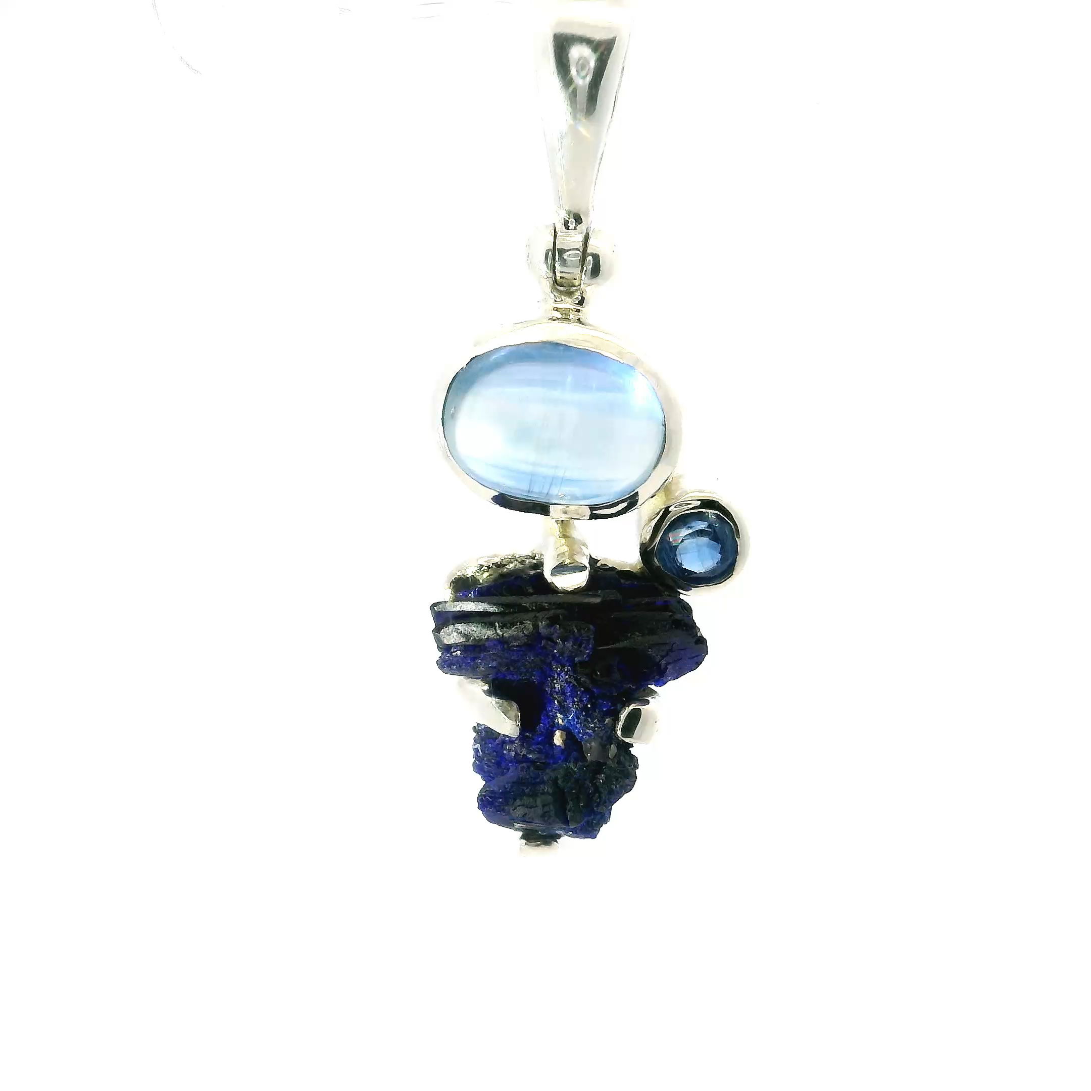 This striking pendant features a raw azurite druzy stone with vivid shades of cobalt and azure, prong-set to highlight its natural texture. Above it, an oval kyanite cabochon adds rich blue depth, while a faceted round gemstone brings a subtle sparkle. Crafted in 925 sterling silver, the polished setting enhances the bold colors and organic shapes. A stunning piece for those who love nature-inspired jewelry, perfect for daily wear or special occasions. Azurite Druze Pendant - Rough Speciman Prong Set with Oval Kyanite Cabochon & Faceted Round Bezel Set in 925 Sterling Silver
