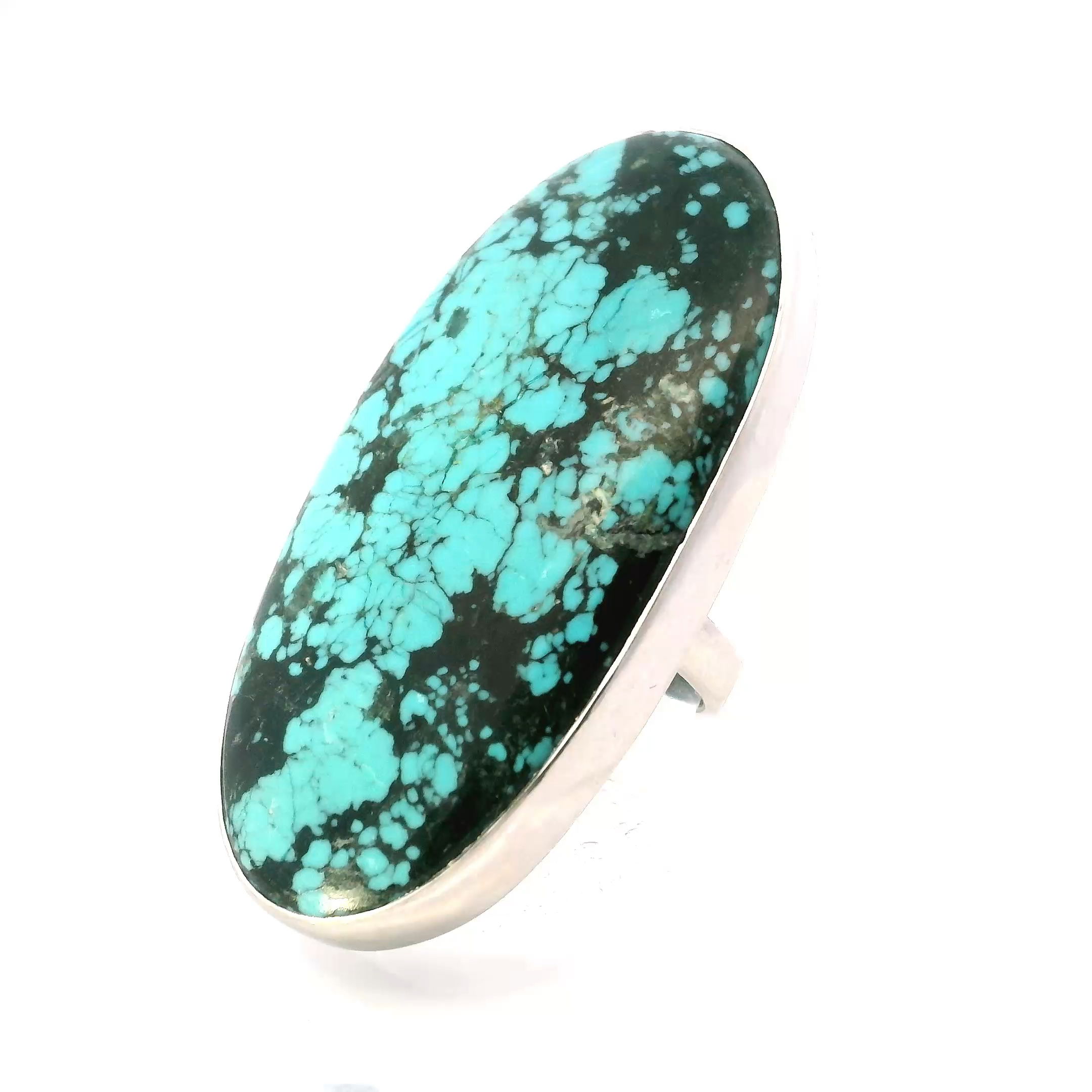 This Tibetan Turquoise Ring features a large oval cabochon with rich blue-green hues and distinctive black inclusions, each stone naturally formed and visually striking. The gemstone is bezel set in a simple 925 sterling silver band, allowing the vivid character of the turquoise to remain the focal point while offering durability and everyday elegance.The band is fully adjustable, accommodating sizes 2 and up, making it as versatile as it is beautiful. With its clean lines and bold centerpiece, this ring adds a grounded, artisanal charm to any look—perfect for those drawn to unique stones and timeless, minimal design. Tibetan Turquoise Ring - Large Oval Cabochon with Black Inclusions Bezel Set in Simple 925 Sterling Silver szAdj 2"+