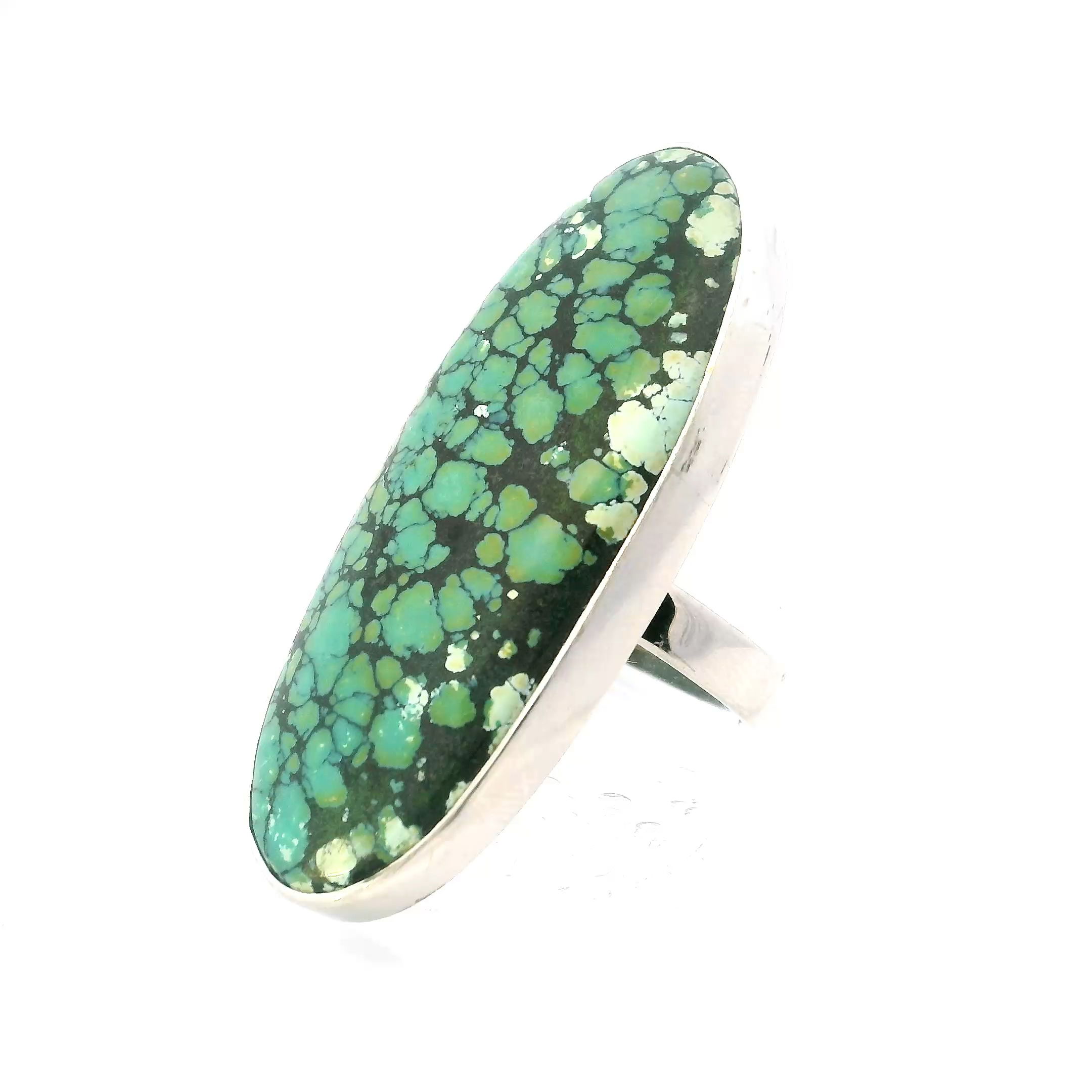 This Tibetan Turquoise Ring features a striking long oval cabochon with vivid blue-green tones and intricate black webbing, each stone a unique expression of natural artistry. Set in a simple 925 sterling silver bezel, the minimalist design highlights the raw beauty of the turquoise while offering lasting strength and elegance.The adjustable band fits from size 1.75 and up, allowing for comfort and flexibility across different fingers and occasions. A timeless piece that bridges earthy tradition with refined style, this ring is ideal for those who value handcrafted detail and the enduring allure of meaningful stones. Tibetan Turquoise Ring - Long Blue-Green Oval Cabochon with Black Webbing Bezel Set in Simple 925 Sterling Silver szAdj 1.75"+