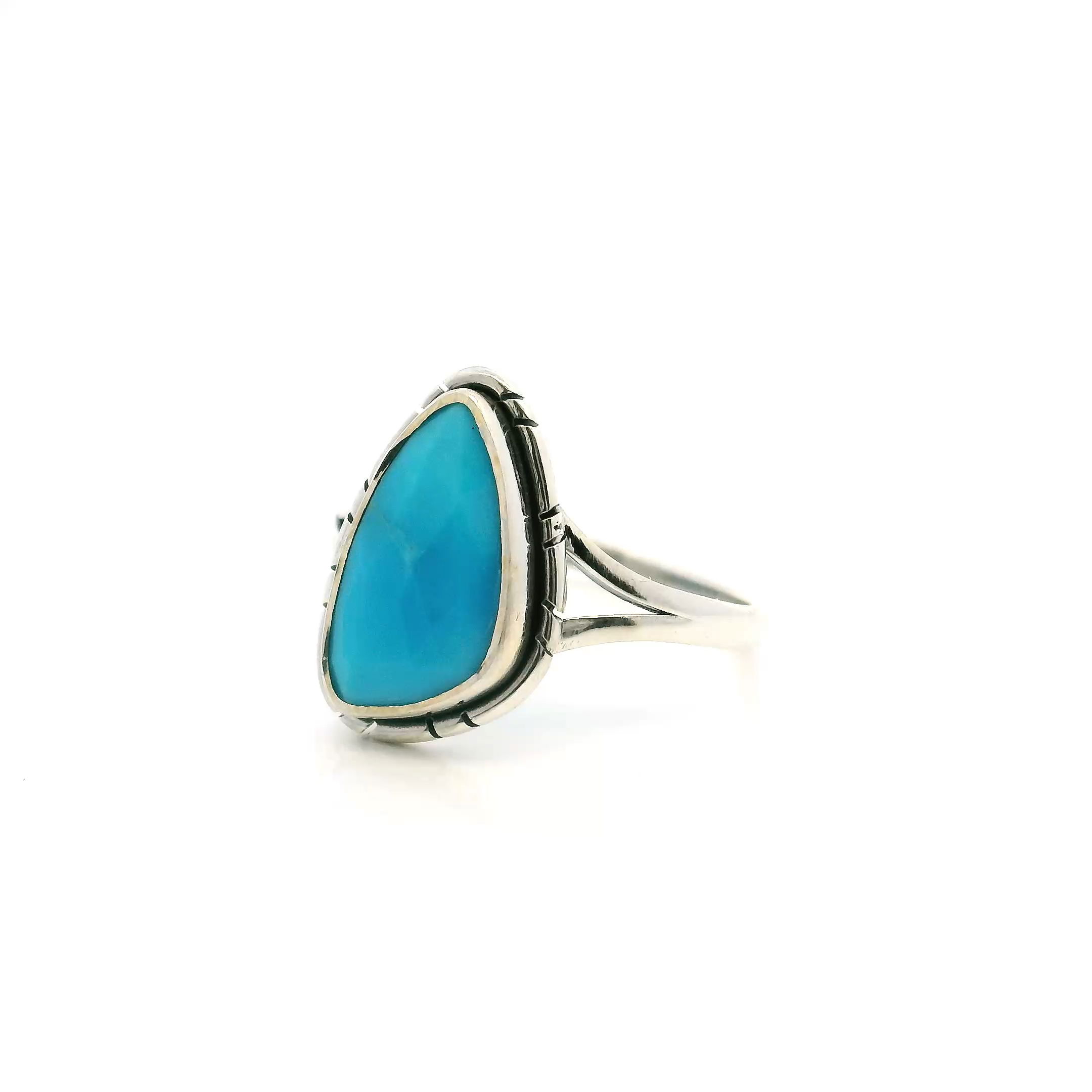 The New Mexican Turquoise Ring features a vibrant, faceted turquoise gemstone, cut into a rounded sideways triangle and bezel set to showcase its captivating hue and natural matrix. Sourced from the renowned mines of New Mexico, each stone is unique, making this ring a true statement piece.Crafted in high-quality 925 sterling silver, the ring’s distinctive double band design offers both comfort and style. Adorned with delicate stamped line details, it reflects the rich craftsmanship of Southwestern jewelry, seamlessly blending modern elegance with traditional flair. New Mexican Turquoise Ring - Faceted Rounded Sideways Triangle Bezel Set with Stamped Line Detail & Double Band in 925 Sterling Silver sz7