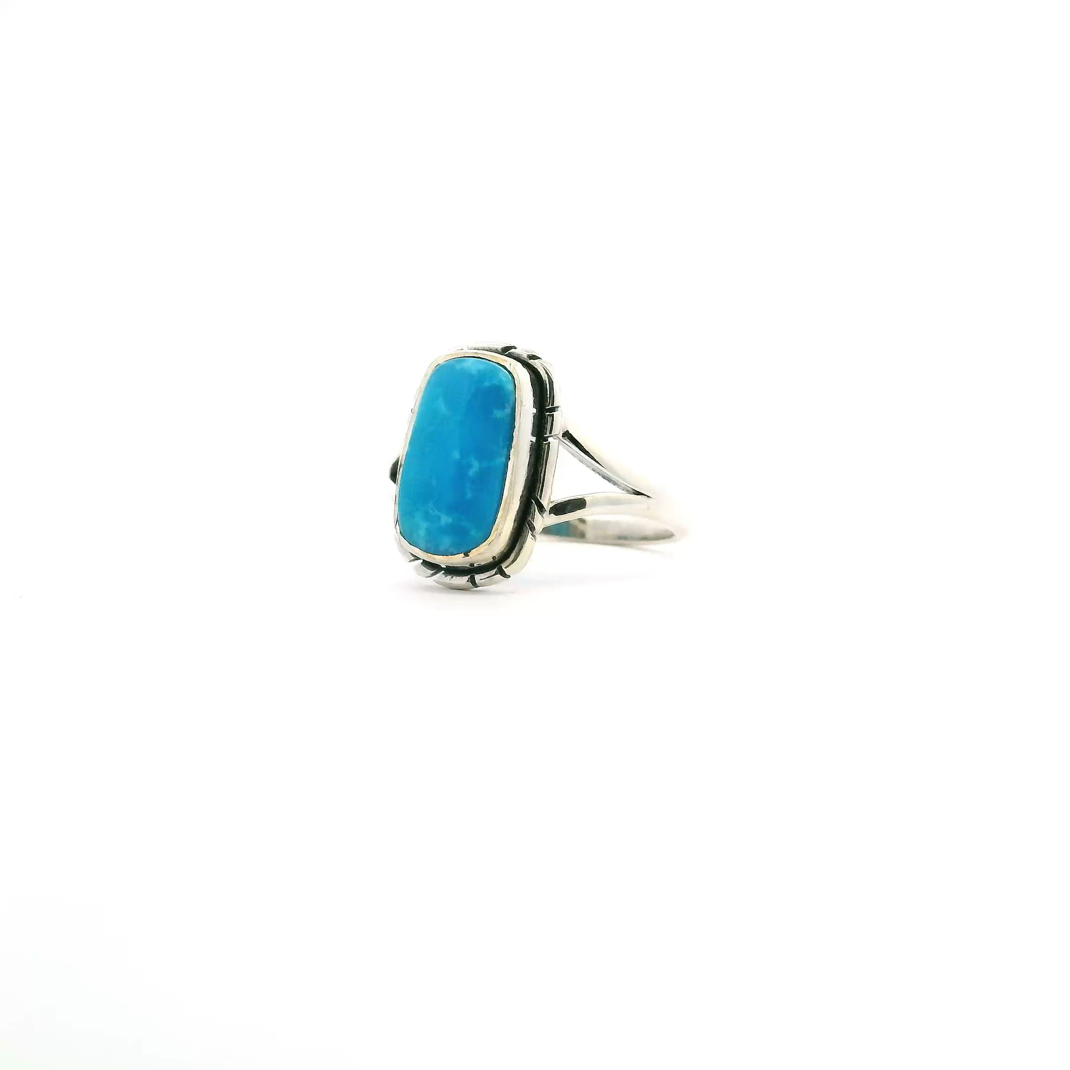 This beautifully crafted ring features a rounded rectangle cabochon of genuine New Mexican turquoise, bezel set in polished 925 sterling silver. Stamped line detailing around the bezel adds artisanal flair, enhancing the stone’s vibrant blue-green tones.Finished with a stylish double band for comfort and stability, this size 5 ring blends timeless Southwestern charm with modern elegance—a striking accessory for any occasion. New Mexican Turquoise Ring - Rounded Rectangle Cabochon Bezel Set with Stamped Line Detail & Double Band in 925 Sterling Silver sz5