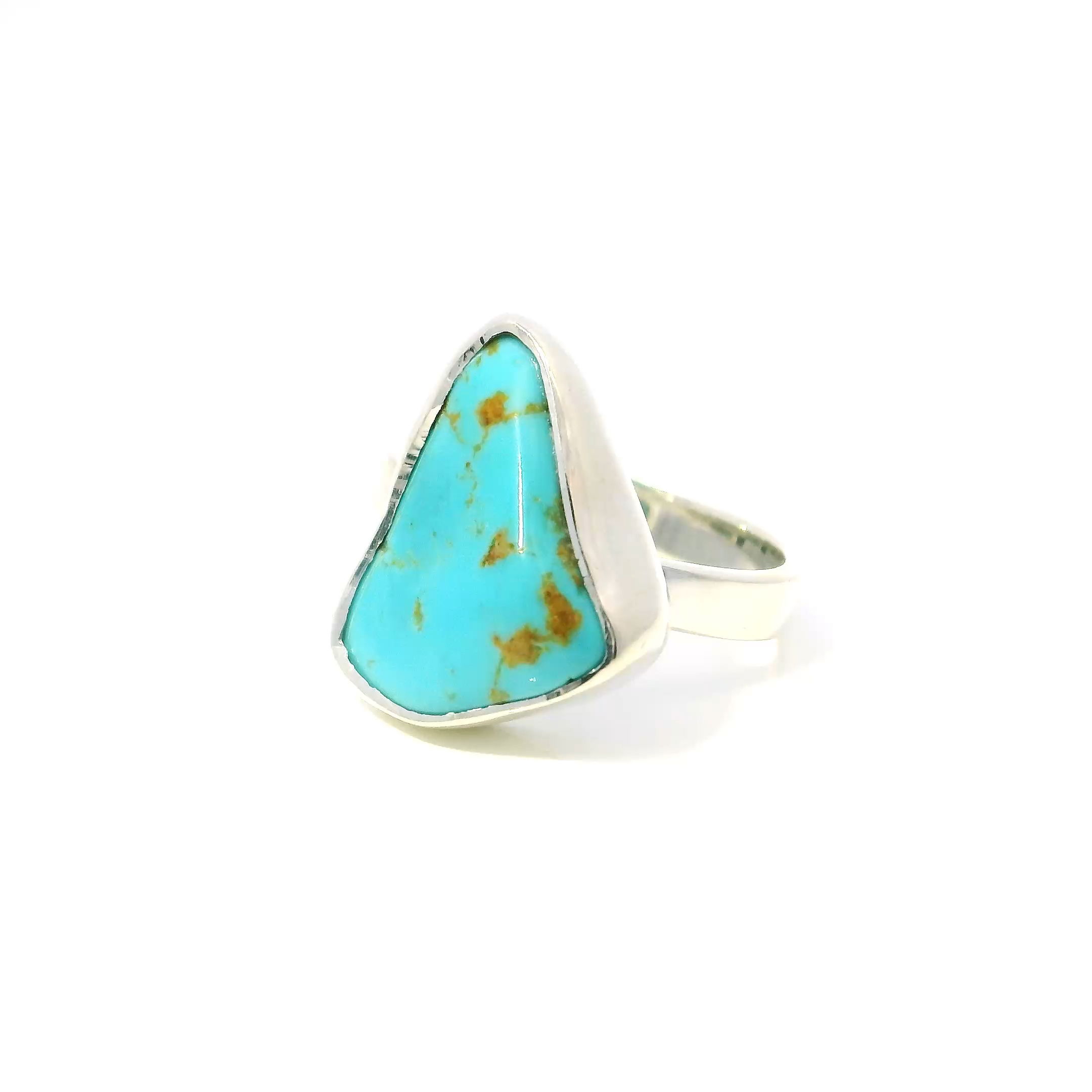 The New Mexican Turquoise Ring features a polished triangular freeform turquoise stone, capturing the rich, calming sea-blue hues and intricate natural patterns unique to New Mexico’s renowned mines. Set in a simple yet elegant 925 sterling silver bezel, the design emphasizes the gemstone’s vibrant color while ensuring durability and timeless style.Sized at 9, this ring blends southwestern allure with modern sophistication, perfect for those who appreciate meaningful jewelry that complements both everyday looks and special occasions. Each piece is uniquely crafted, making it a treasured symbol of natural beauty and cultural heritage. New Mexican Turquoise Ring - Polished Triangular Freeform Bezel Set in Simple 925 Sterling Silver sz9