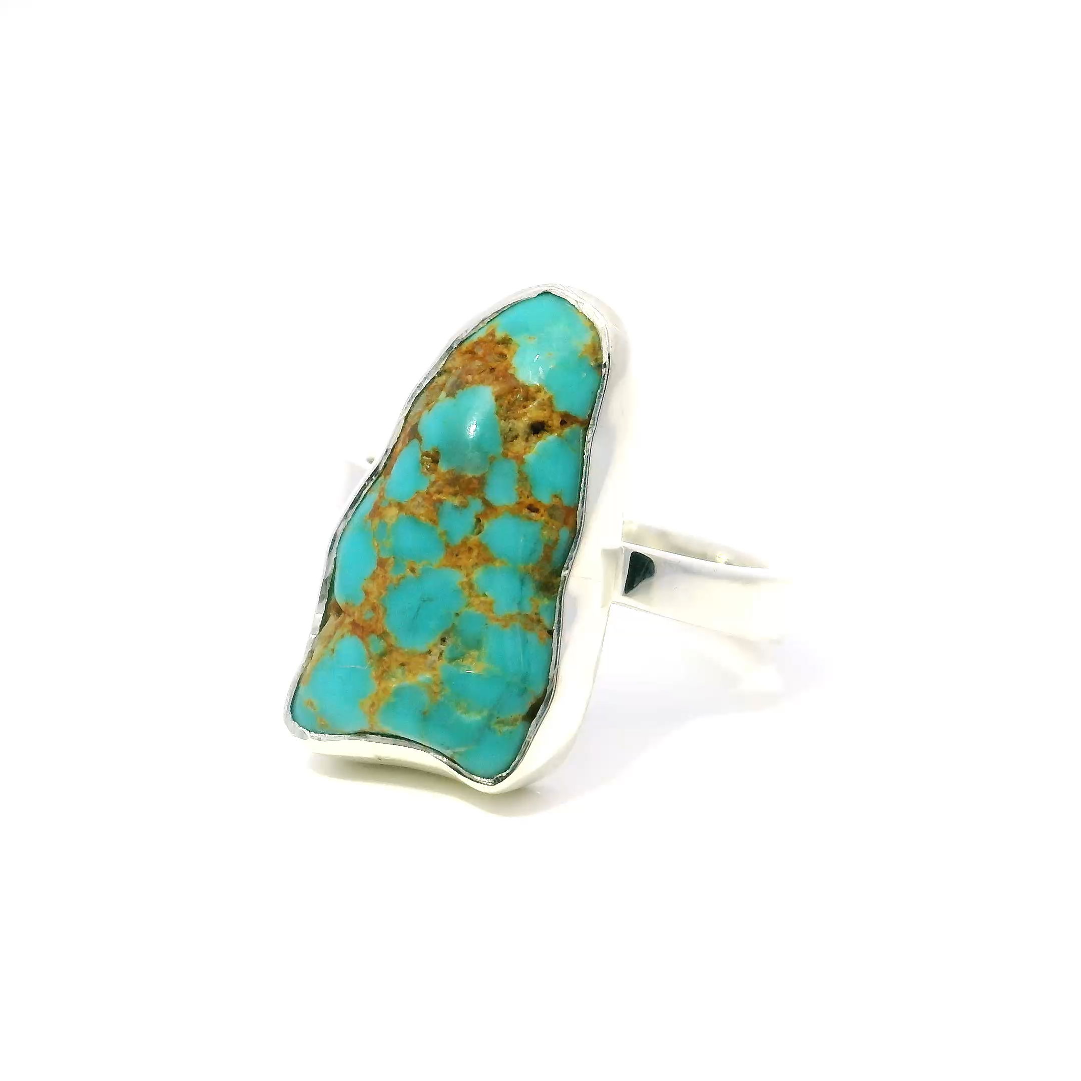 The New Mexican Turquoise Ring features a polished triangular freeform turquoise stone with vibrant blue hues and distinctive tan inclusions that highlight its natural origin. The stone is bezel set in simple 925 sterling silver, creating a balanced design that emphasizes the unique beauty of the turquoise. Sized at 10, this ring offers a comfortable fit and a bold, timeless style.Crafted to combine natural charm with refined craftsmanship, this piece suits those who appreciate authentic, one-of-a-kind jewelry. Its clean silver setting and striking turquoise make it an elegant addition to any collection or a meaningful gift for someone who values understated sophistication. New Mexican Turquoise Ring - Polished Triangular Freeform with Multiple Tan Inlcusions Bezel Set in Simple 925 Sterling Silver sz10