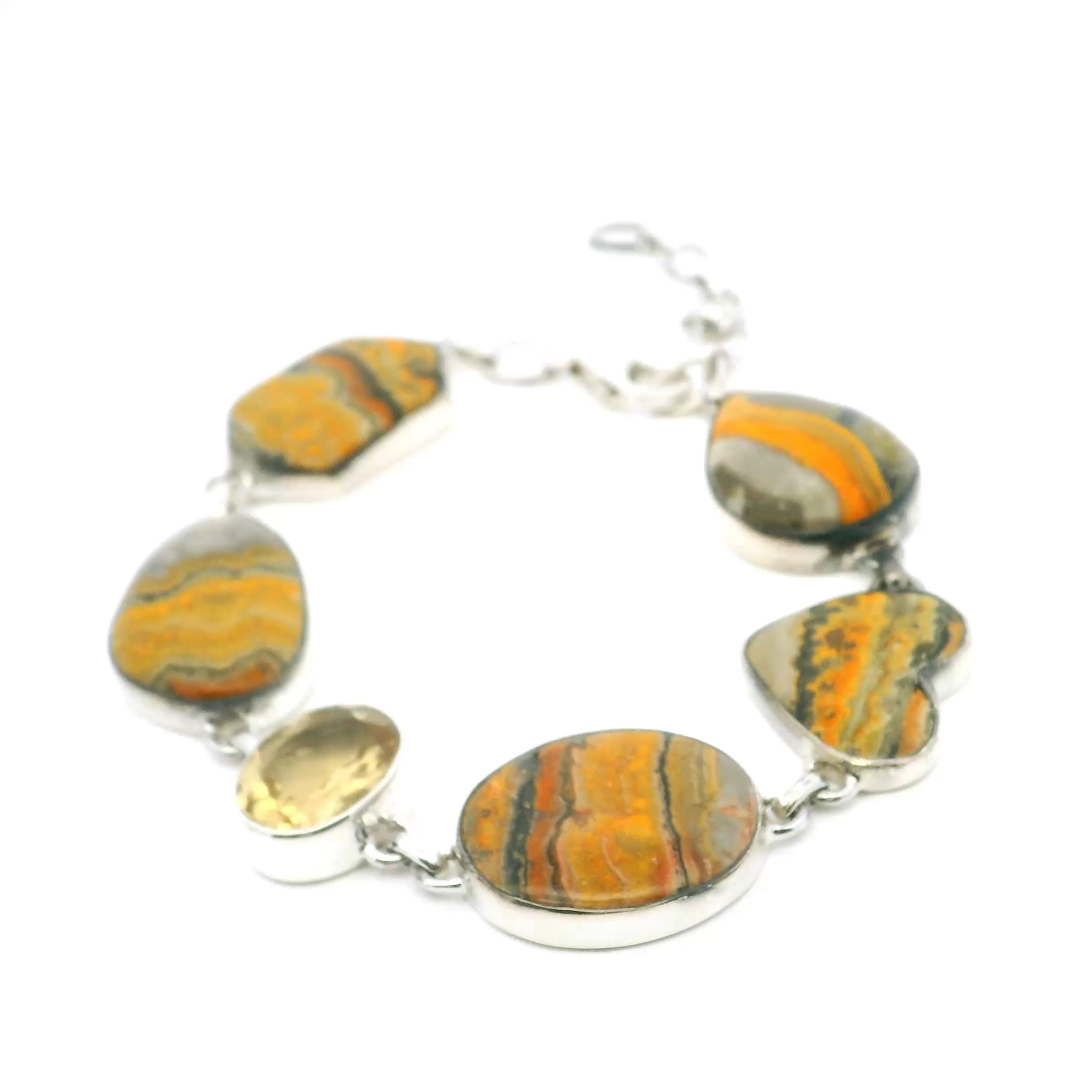This Bumblebee Jasper Link Bracelet with Citrine Accents in 925 Sterling Silver is a radiant composition of color, texture, and form, designed to capture the fiery elegance of natural stone. A striking arrangement of pear, heart, oval, and hexagon-shaped cabochons of bumblebee jasper spans the wrist, each stone alive with golden yellows, deep charcoal veining, and vibrant orange striations. Between them, bezel-set faceted oval citrines add a warm, honeyed sparkle that enhances the jasper’s volcanic palette.Set in cool, polished sterling silver, each link is articulated for graceful movement and balanced weight. The secure clasp ensures a comfortable fit, making this piece as wearable as it is bold. Ideal for women who seek jewelry with character, this bracelet blends organic richness with refined craftsmanship, offering a statement of style that feels both grounded and luminous. Bumblebee Jasper Link Bracelet - Pear, Heart, Oval & Hexagon Cabochons with Faceted Citrine Oval Bezel Set in 925 Sterling Silver
