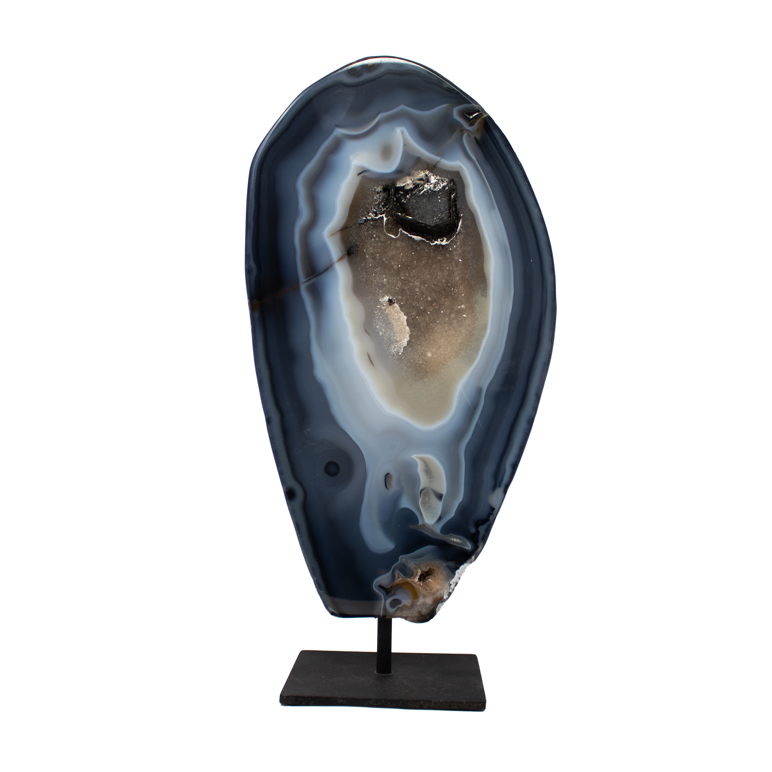 The Agate Druze Geode on Post Stand from Brazil is a striking fusion of raw elegance and refined presentation, showcasing deep navy agate with intricate natural banding and a rare inclusion of dissolved calcite crystals. Black druze accents glimmer across its surface, catching light with every shift and adding a celestial shimmer to its already captivating form.Mounted on a minimalist black post stand, this geode becomes both a sculptural centerpiece and a grounding presence—perfect for desktops, mantels, or crystal collections. Sourced from Brazil’s renowned mineral-rich regions, each piece is entirely unique, a one-of-a-kind expression of Earth’s artistry. Agate’s stabilizing energy and the sparkle of druze combine to create a piece that is as energetically uplifting as it is visually stunning. Agate Druze Geode on Post Stand from Brazil with Navy Agate & Dissolved Calcite Crystal Inclusion of Black Druze