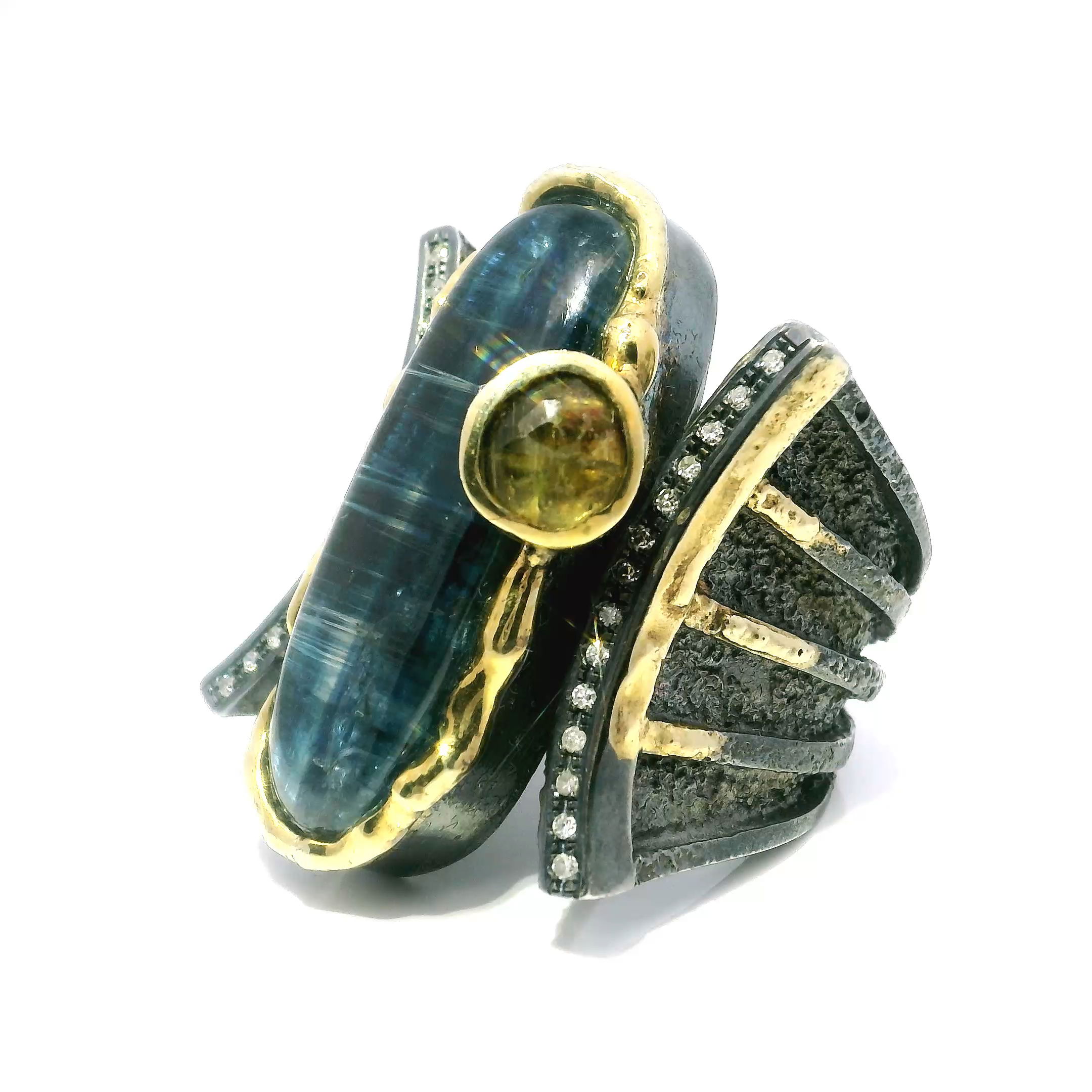 Elevate your look with this striking Kyanite Ring in 925 Sterling Silver, designed to captivate. A long oval blue kyanite cabochon takes center stage, bezel-set to showcase its silken depth and natural allure. Above it, a golden tourmaline sparkles with faceted brilliance, framed by gracefully arcing rows of pave-set diamonds.Dripped gold accents add richness and textural contrast, enhancing the sculptural elegance of the design. Crafted in size 9.5, this piece is a wearable work of art—perfect for those who appreciate bold gemstones, intricate detailing, and statement-making style. Kyanite Ring - Long Oval Cabochon & Faceted Golden Tourmaline Round Between 2 Curved Lines of Single Row Pave Diamonds with Dripped Gold Accents Bezel Set in 925 Sterling Silver sz9.5