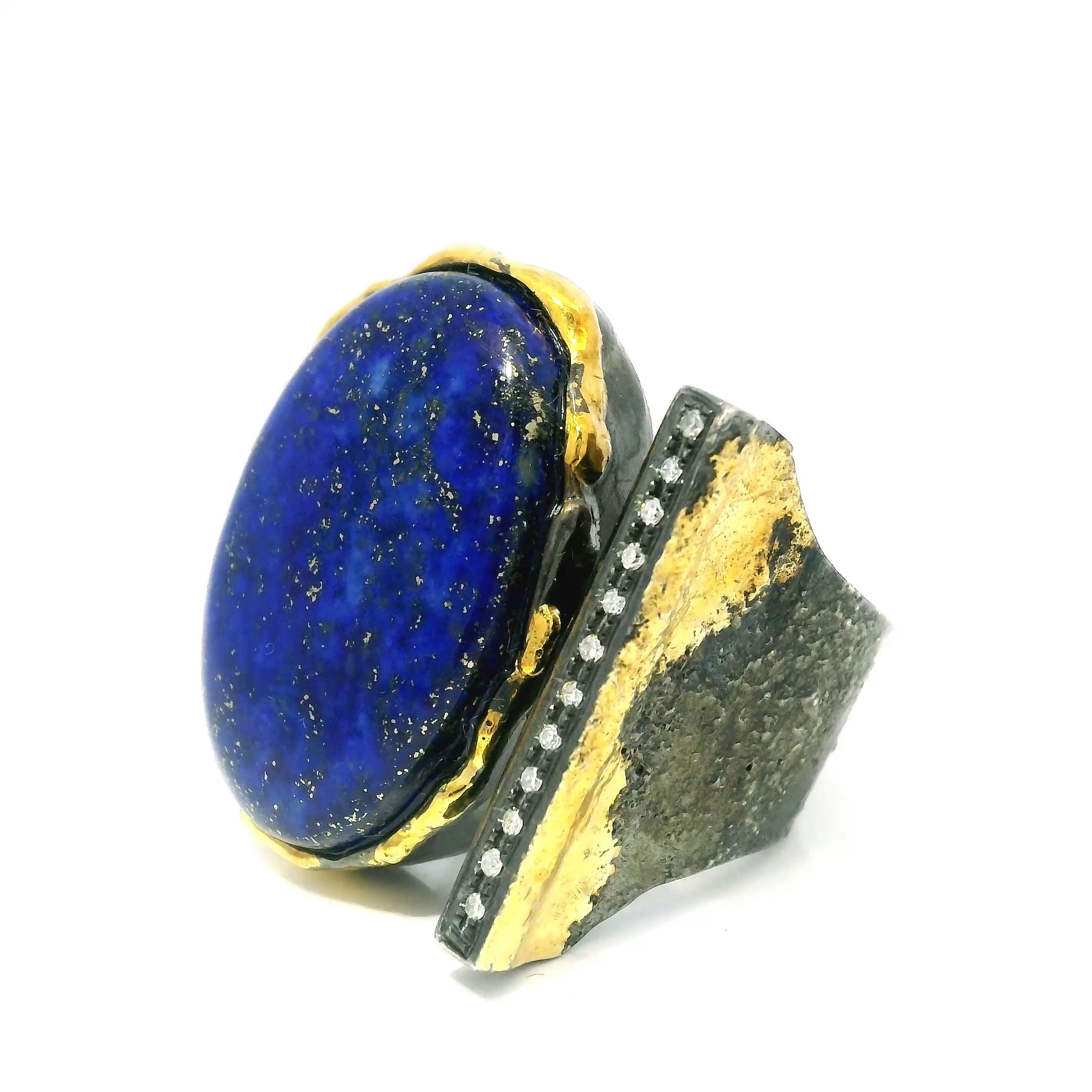 Elevate your style with this stunning Lapis Lazuli Ring, featuring a mesmerizing oval cabochon at its center. The deep blue gemstone is bezel set in gleaming 925 sterling silver, while dripped gold accents artfully frame the stone for a touch of opulence. A single row of pavé-set diamonds sparkles along the open band, adding refined brilliance to this elegant piece.Designed in a classic size 7, this ring is a true statement of sophistication—perfect for any occasion. Indulge in timeless beauty and distinctive craftsmanship with a piece that blends natural elegance and modern artistry in perfect harmony. Lapis Lazuli Ring - Oval Cabochon on Open Band with Single Row Pave Diamonds & Dripped Gold Accents Bezel Set in 925 Sterling Silver sz7