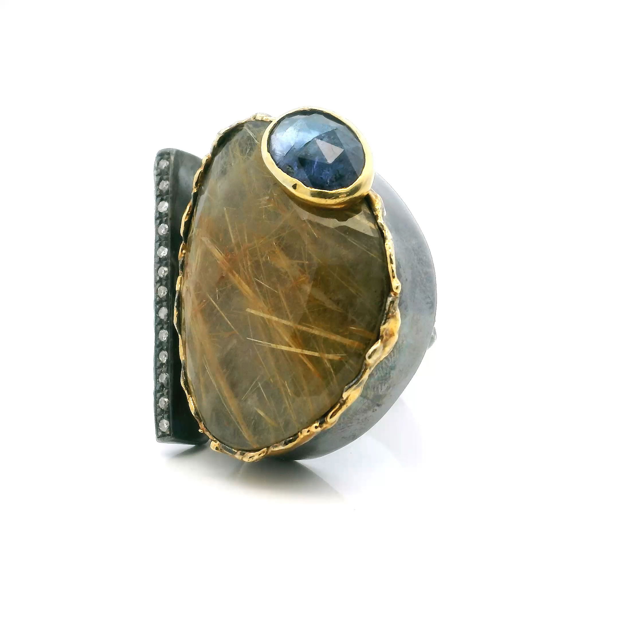 Elevate your jewelry collection with this striking Golden Rutilated Quartz Ring, expertly crafted in 925 sterling silver. A captivating faceted triangle of golden rutilated quartz takes center stage, paired with an alluring faceted oval of deep iolite for a sophisticated contrast of color and texture.The open band design is adorned with a single row of shimmering pavé diamonds, while dripped gold accents and refined bezel settings highlight the unique character of each gemstone. Sized at 8.5, this modern yet timeless piece offers bold artistry and elegance—perfect for elevating both everyday wear and special occasion ensembles. Golden Rutilated Quartz Ring - Faceted Triangle & Faceted Iolite Oval on Open Band with Single Row Pave Diamonds & Dripped Gold Accents Bezel Set in 925 Sterling Silver sz8.5