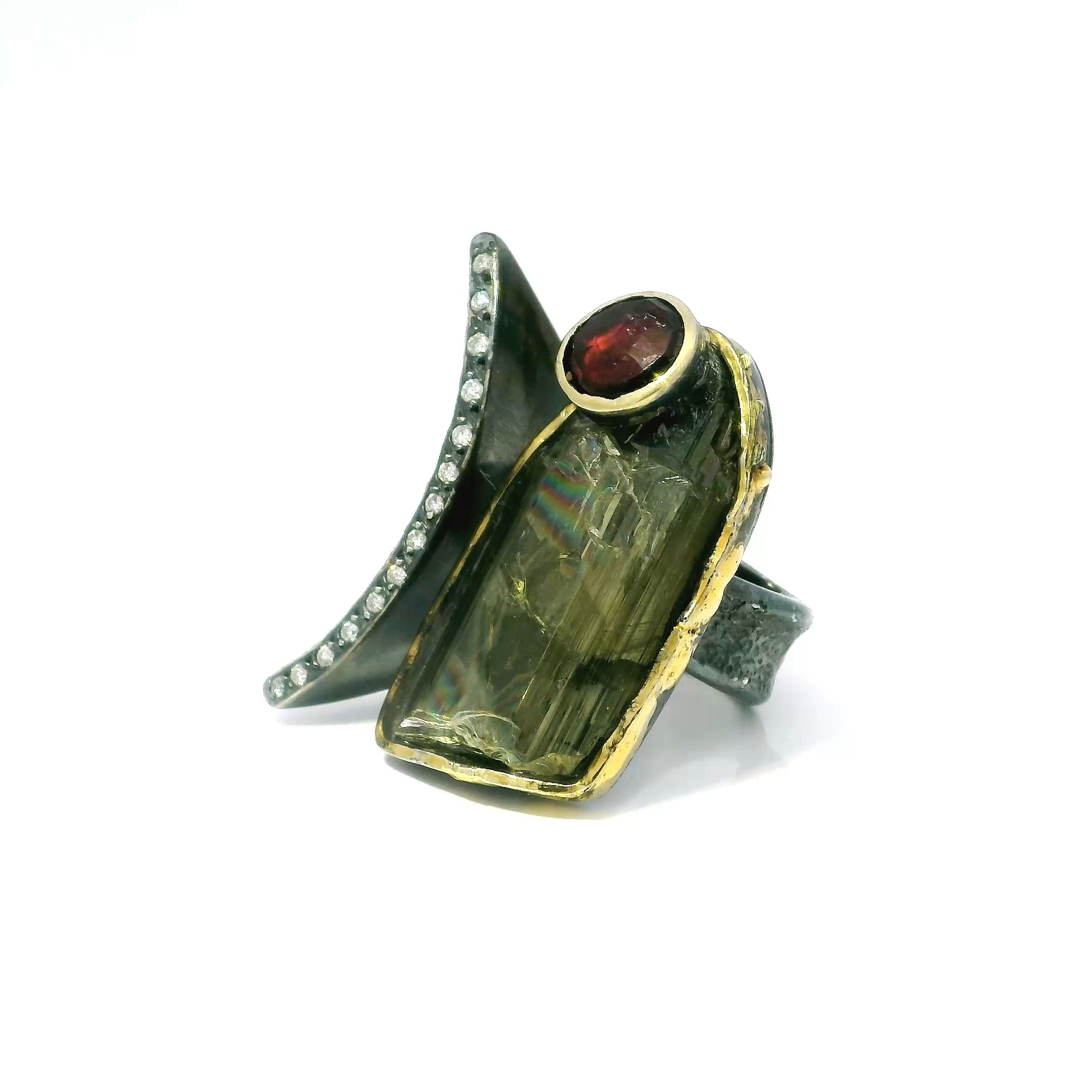Make a bold statement with this one-of-a-kind Zultanite Ring, showcasing a shield-shaped freeform zultanite that shifts effortlessly from olive green to rosy champagne under changing light. This rare, color-changing gemstone is bezel set in luminous 925 sterling silver, offering a sleek and secure frame that enhances its natural beauty.Complementing the zultanite is a brilliant faceted round pink tourmaline, adding a vibrant pop of contrast. A single row of pavé-set diamonds arcs along the open band, while dripped gold bezel accents introduce warmth and modern texture. Designed in size 9, this ring is a striking blend of elegance and artistry—an unforgettable addition to any fine jewelry collection. Zultanite Ring - Shield Freeform & Faceted Pink Tourmaline Round on Open Band with Single Row Pave Diamonds & Dripped Gold Accents Bezel Set in 925 Sterling Silver sz9