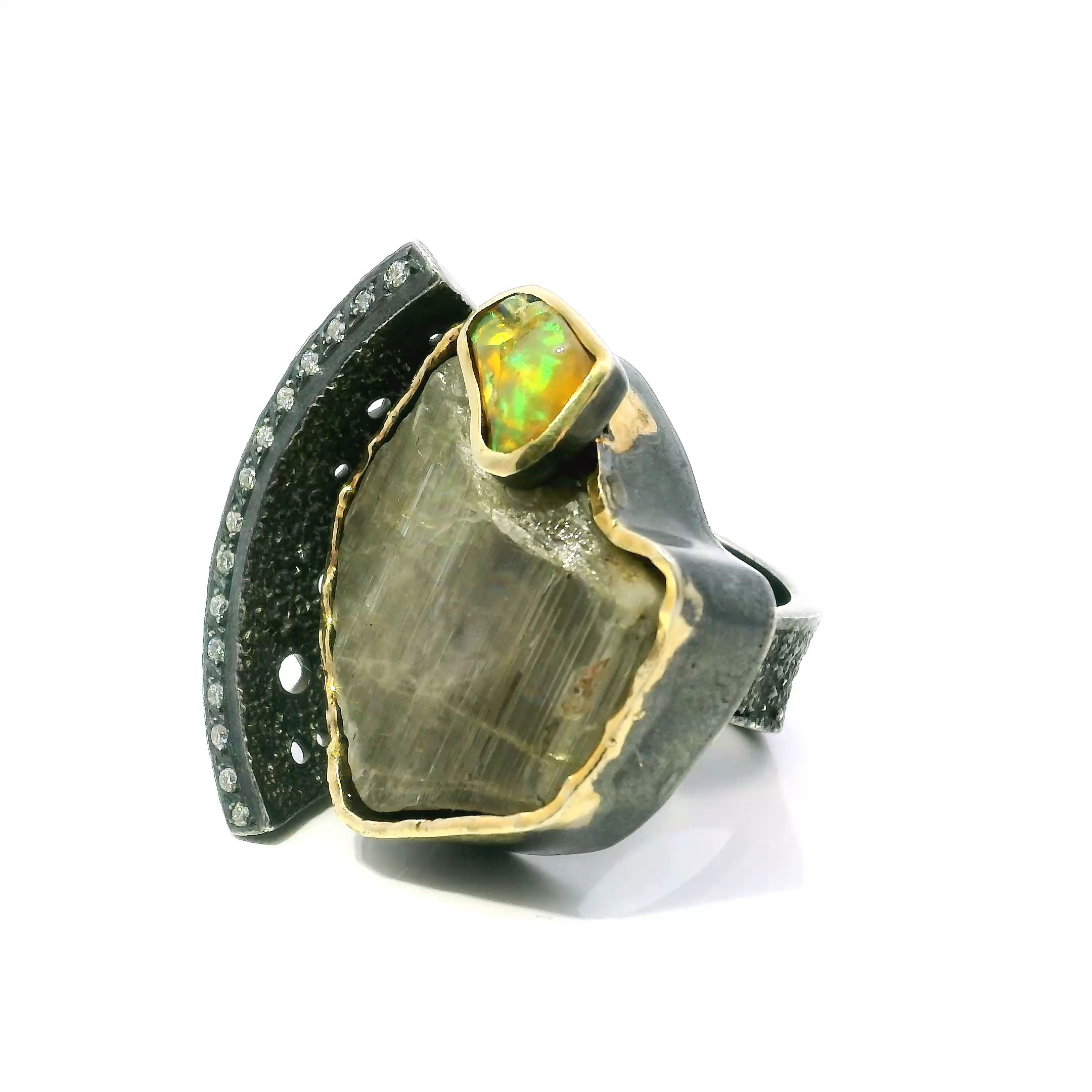 Discover the mesmerizing allure of our Zultanite Ring, meticulously crafted with a striking triangular freeform Zultanite known for its captivating color-changing properties. Paired with an ethereal freeform Ethiopian Opal, both stones are bezel set to showcase their unique brilliance and character.The open band, crafted in luminous 925 sterling silver, features a single row of sparkling pavé-set diamonds tracing elegant curves. Dripped gold accents highlight the bezels, adding a sophisticated contrast and artisanal flair. Sized for a comfortable size 7 fit, this ring blends modern artistry with organic beauty, making it a standout addition to any fine jewelry collection. Zultanite Ring - Triangular Freeform & Freeform Ethiopian Opal on Open Band with Single Row Pave Diamonds & Dripped Gold Accents Bezel Set in 925 Sterling Silver sz7