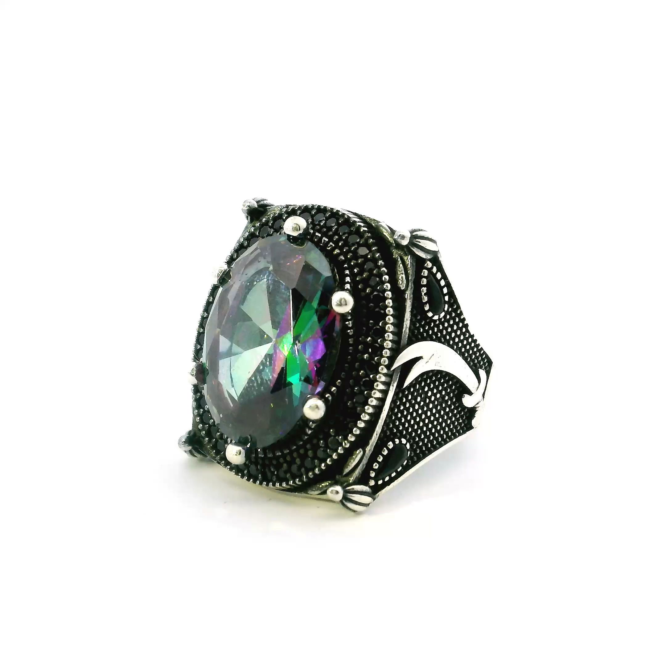 Unleash a bold statement with this Mystic Topaz Ring, uniquely crafted for those who thrive on individuality. The faceted oval mystic topaz mesmerizes with a rainbow of hues, encircled by a single row of glinting black nanostones that invite intrigue and admiration.The sterling silver band, sized 11.5, features a striking cutlass sword motif—evoking daring adventures and resilience—while the detailed beaded crown prong setting offers regal security for the central stone. This unforgettable piece elevates any men’s jewelry collection where artistry, strength, and mystique converge. Mystic Topaz Ring - Faceted Oval Surrounded by Single Row Pave Black Nanostones & Cutlass Sword on Band with Beaded Crown Prong Setting in 925 Sterling Silver sz11.5