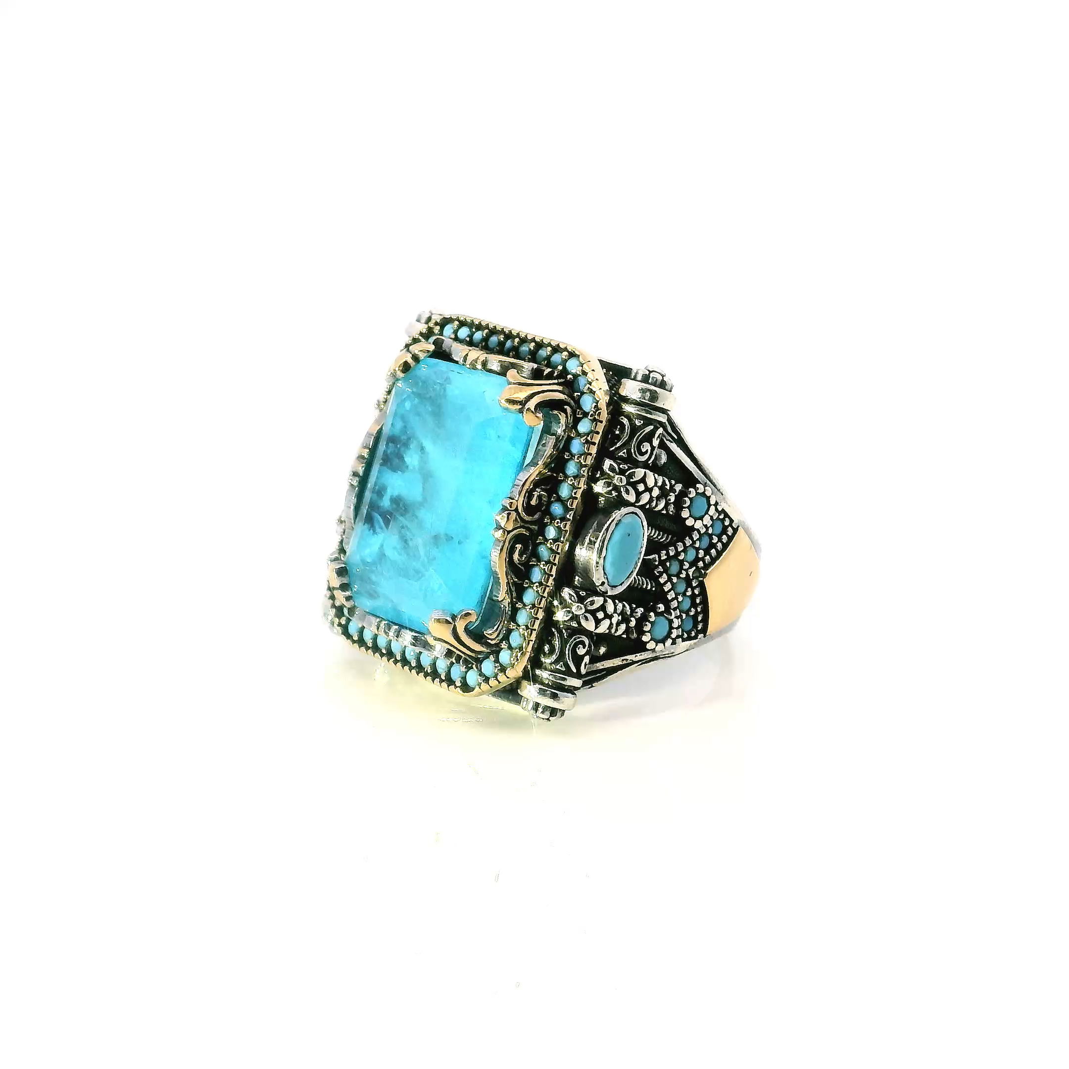 Elevate your style with this distinctive Aquamarine Ring, crafted for those who value bold sophistication and unique design. The centerpiece features a faceted rectangle aquamarine, shimmering with icy brilliance as it catches the light. It's framed by a radiant row of vivid pavé turquoise nanostones that add striking color and modern flair.Flanked by two faceted oval turquoise stones, the composition is further enhanced by ornate scroll accents and elegant prong settings, all sculpted in solid 925 sterling silver and finished with rich gold vermeil. Designed in size 11.75, this standout piece blends artistic craftsmanship with contemporary elegance—an unforgettable addition to any jewelry collection. Aquamarine Ring - Faceted Rectangle with Single Row Pave Turquoise Nanostones & 2 Faceted Turquoise Side Ovals & Scroll Accents Fancy Prong Set in 925 Sterling Silver with Gold Vermeil Accents sz11.75