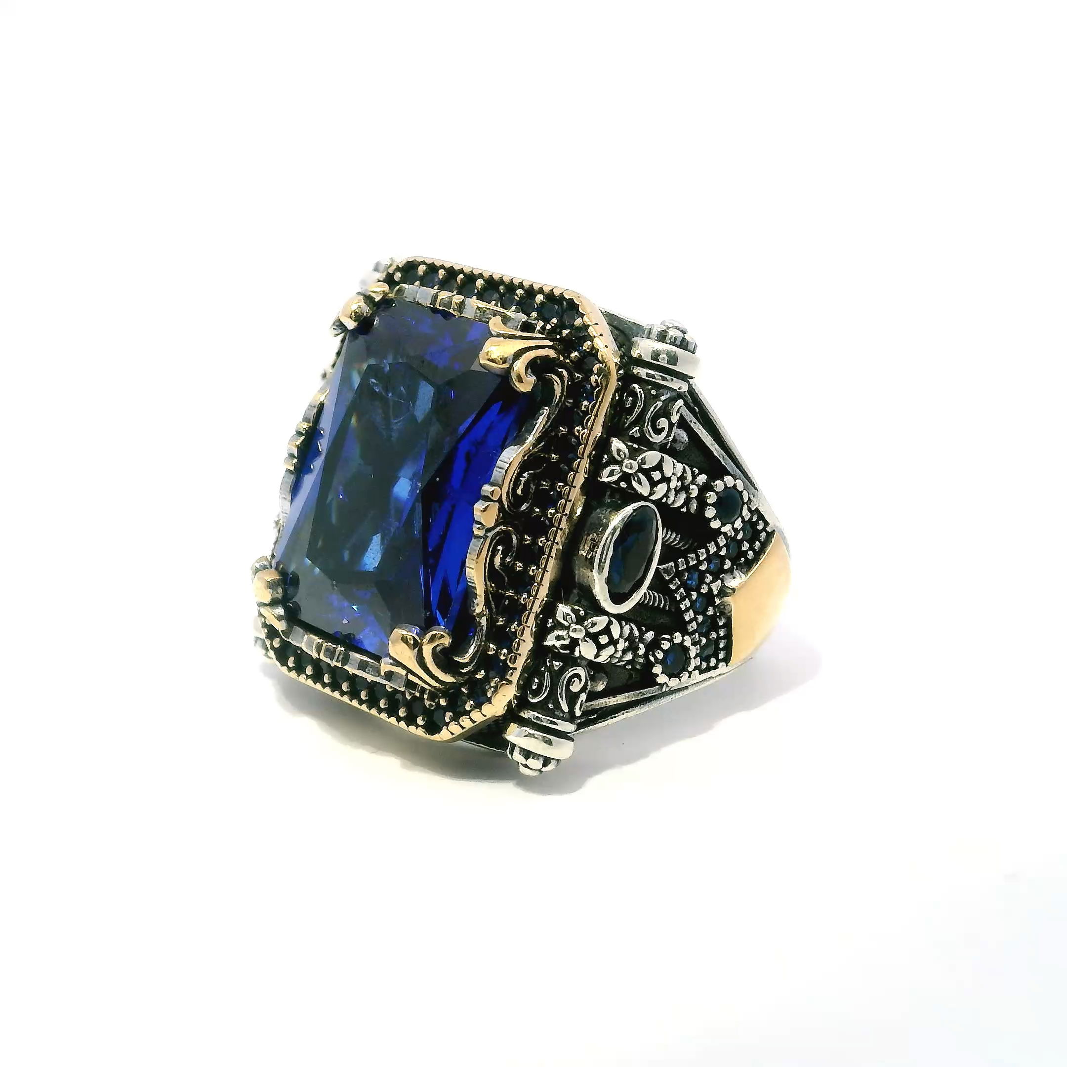 Make a bold statement with this exquisite Sapphire Ring—an inspired fusion of tradition and innovation. At its center, a faceted rectangular sapphire radiates depth and brilliance, secured in a detailed prong setting. Two richly hued faceted sapphire ovals flank the centerpiece, while a single row of pave-set sapphire nanostones adds a refined touch of sparkle.Intricate scrollwork accents the band, complemented by warm gold vermeil highlights over solid 925 sterling silver. Designed in size 10.5, this ring offers a balance of craftsmanship, durability, and timeless style—perfect for anyone seeking a distinctive piece to elevate their jewelry collection. Sapphire Ring - Faceted Rectangle with Single Row Pave Sapphire Nanostones & 2 Faceted Sapphire Side Ovals & Scroll Accents Fancy Prong Set in 925 Sterling Silver with Gold Vermeil Accents sz10.5