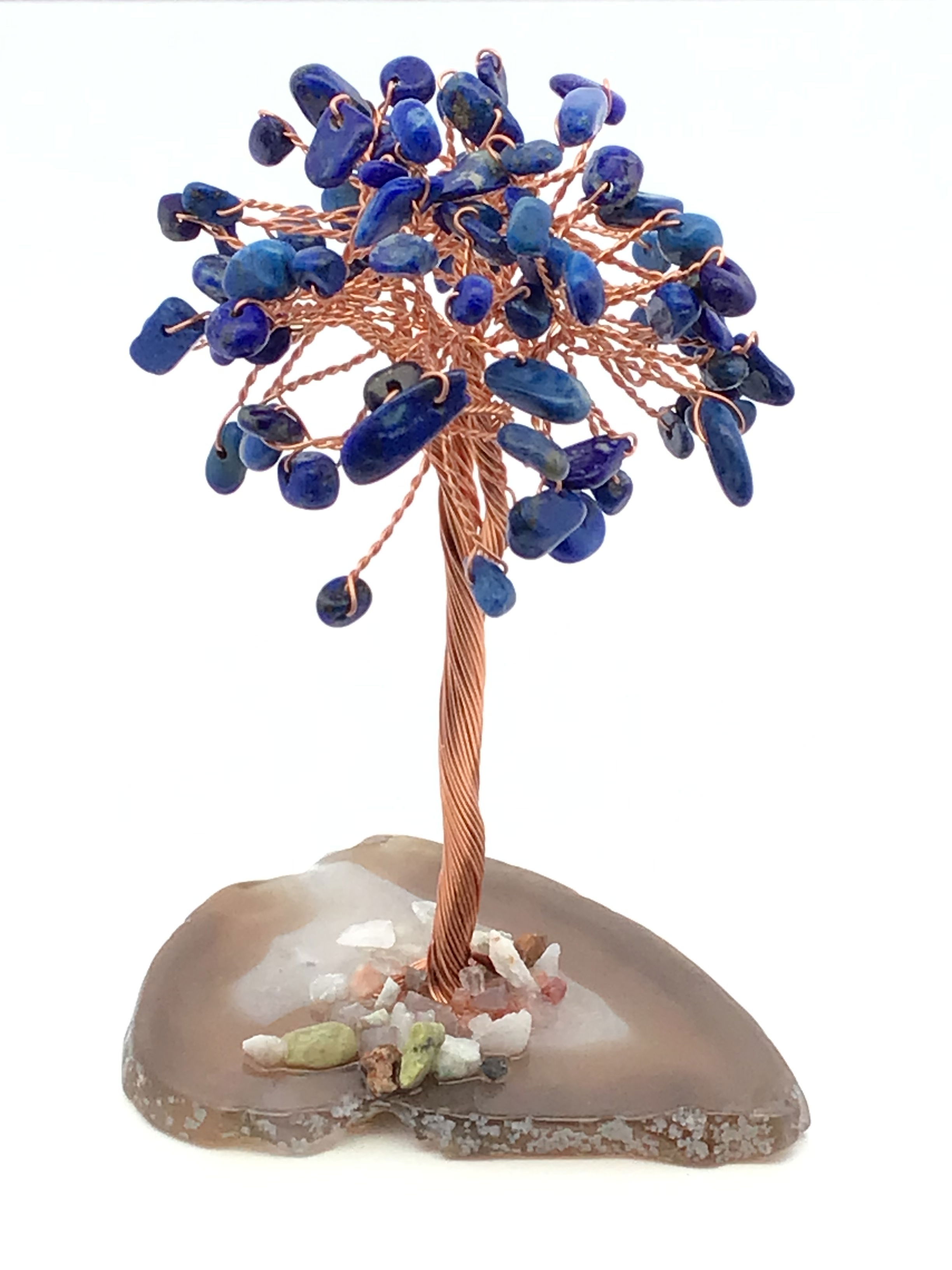 Discover the enchanting beauty of our Lapis Lazuli Copper Wire Beaded Tree on Agate Base—a captivating fusion of natural gemstones and artisanal craftsmanship. Hand-twisted copper branches shimmer with vibrant Lapis Lazuli gemstone leaves, radiating depth, wisdom, and celestial charm. Each leaf is carefully beaded for a lifelike, organic form that brings movement and energy to the piece.Rooted in a polished agate base, every tree is grounded in swirling bands of natural color, making each one a unique treasure. Ideal as a meditation tool, home centerpiece, or gift for a crystal enthusiast, this piece adds elegance and serenity to any space. Lapis Lazuli Copper Wire Beaded Tree on Agate Base
