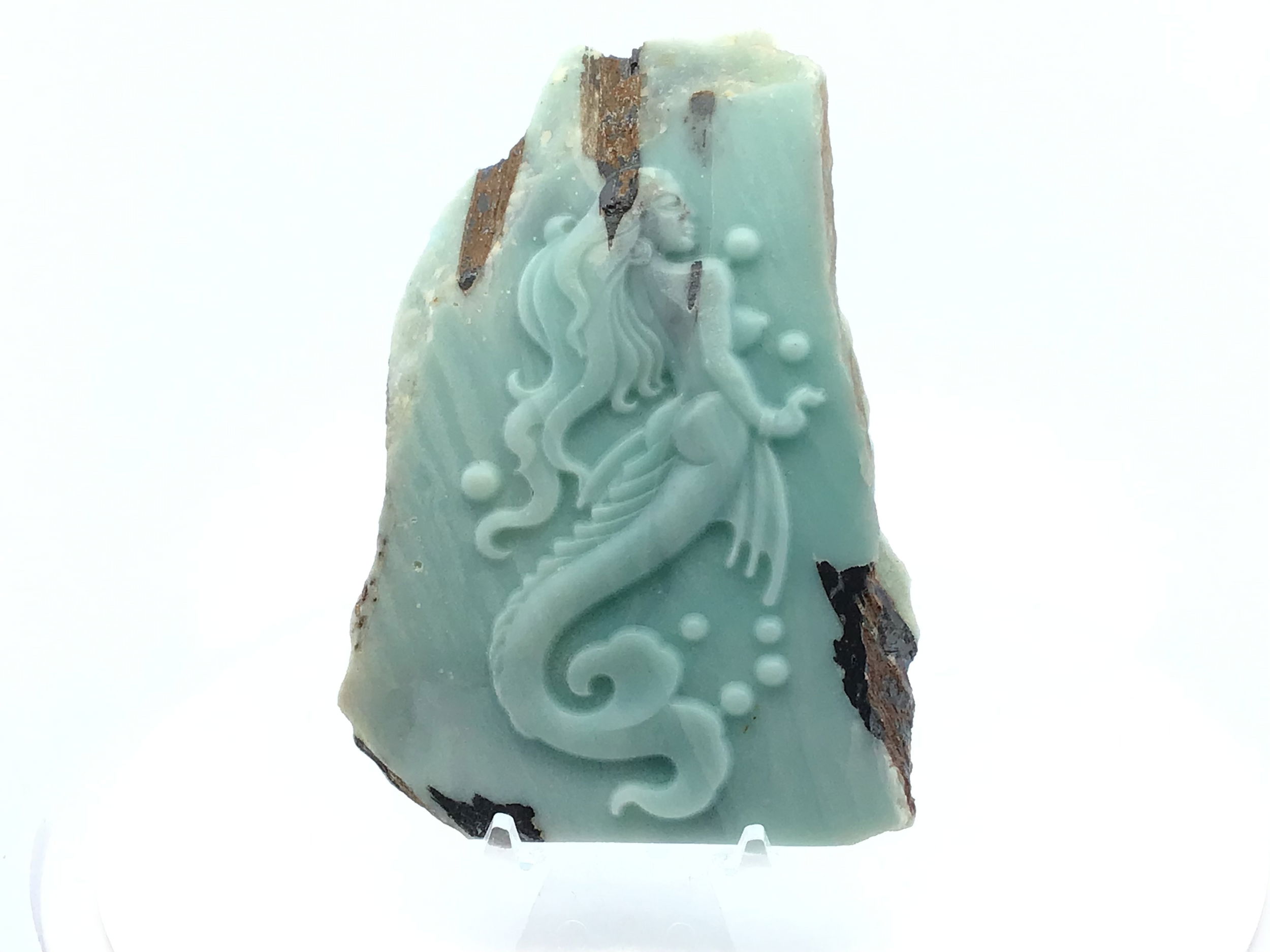 Hand-carved from premium A+ Amazonite, this enchanting mermaid figure captures the ocean’s grace in sculptural form. Her flowing hair, delicate fins, and serene posture are carved with exquisite detail, each curve echoing the fluidity of water. Resting on a crystal-clear Lucite stand, the piece appears to float, enhancing its ethereal presence on any shelf, desk, or altar.The soothing blue-green tones of Amazonite evoke tranquil seas and coastal skies, making this carving not only a visual delight but also a symbol of calm, creativity, and feminine strength. Perfect for collectors, dreamers, or as a meaningful gift, this Amazonite Mermaid infuses any space with oceanic magic and natural beauty. A+ Amazonite Mermaid Carving with Lucite Stand